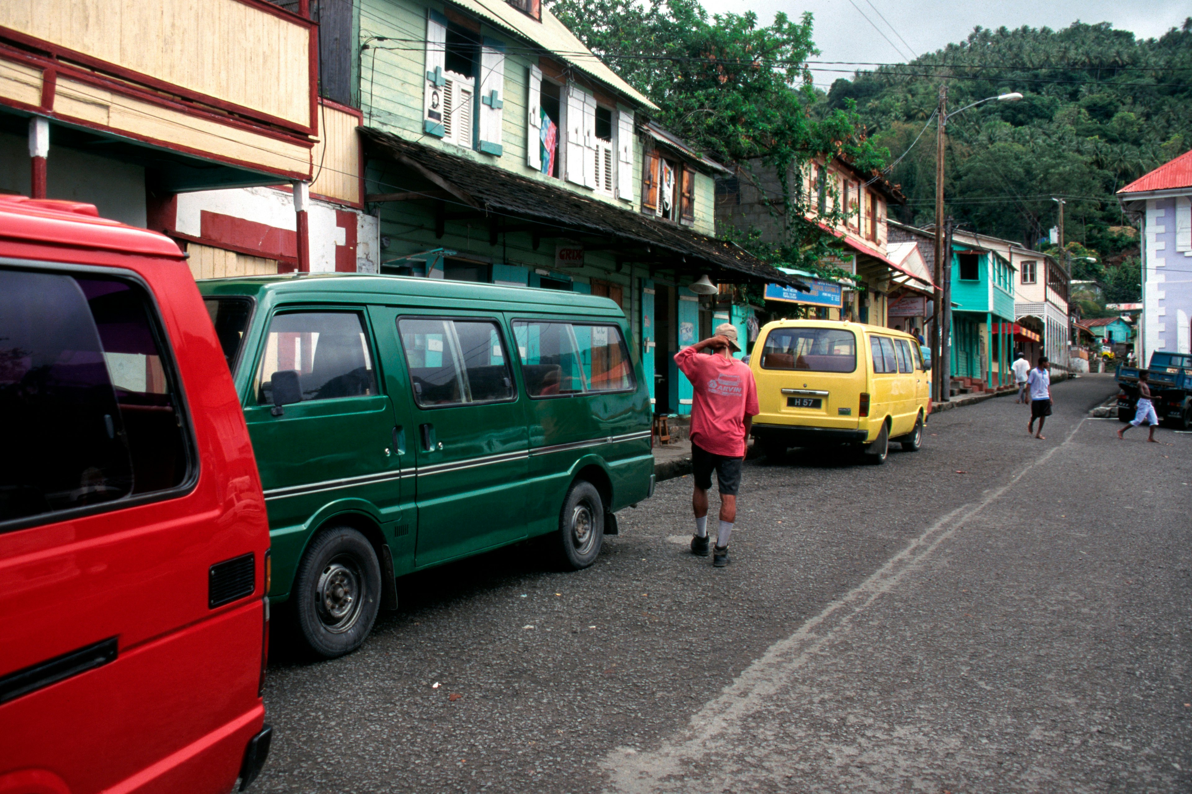 A man walks past a trio of brightly colored taxis on a busy road in St Lucia