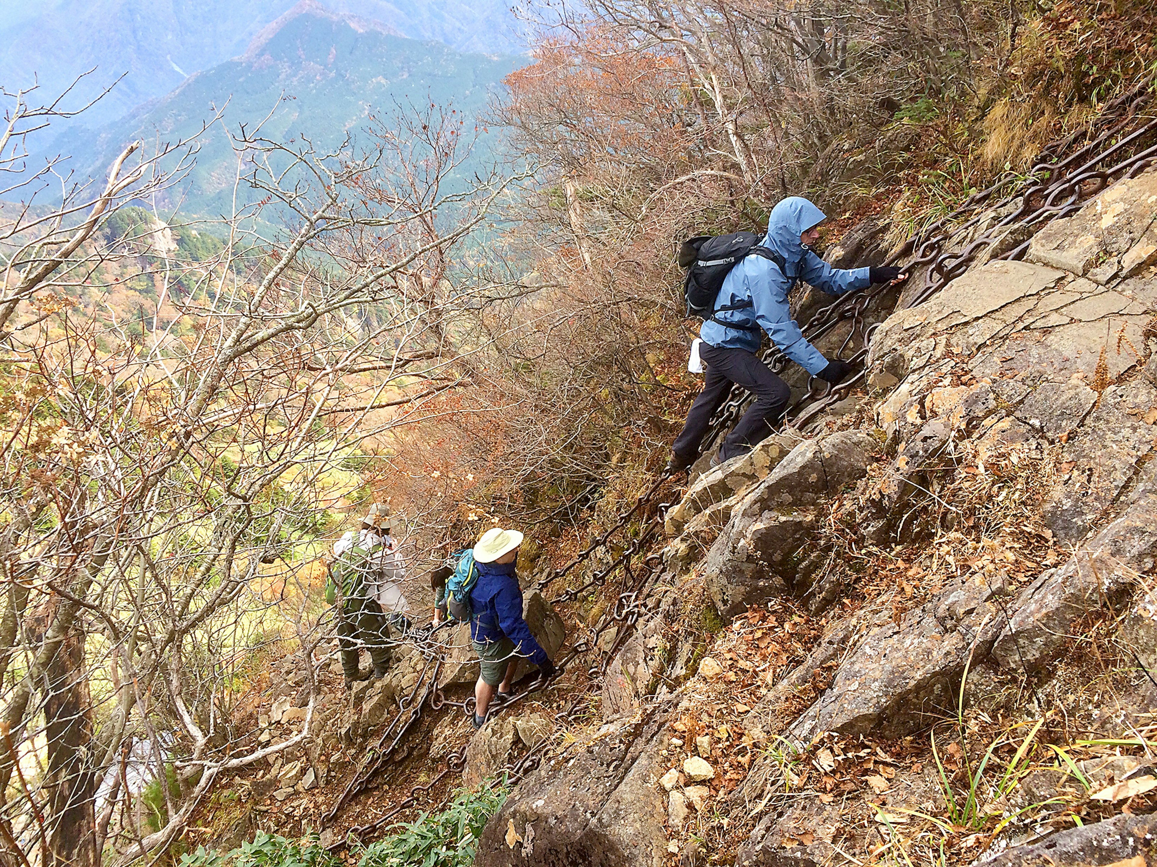 Climbers using chains to pull themselves up a steep, rocky slope