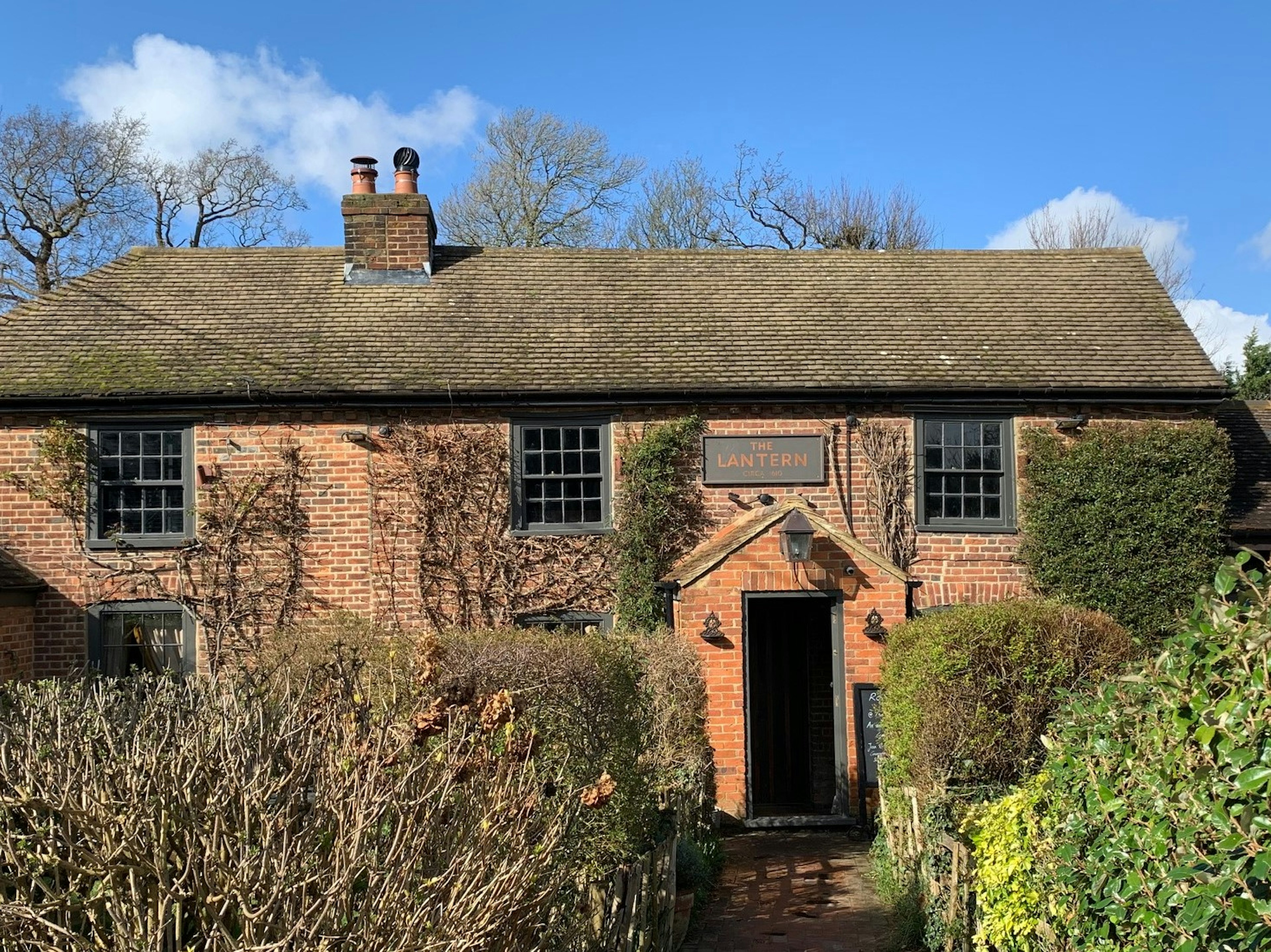 The red-brick exterior of the Lantern Inn, with hedges in front