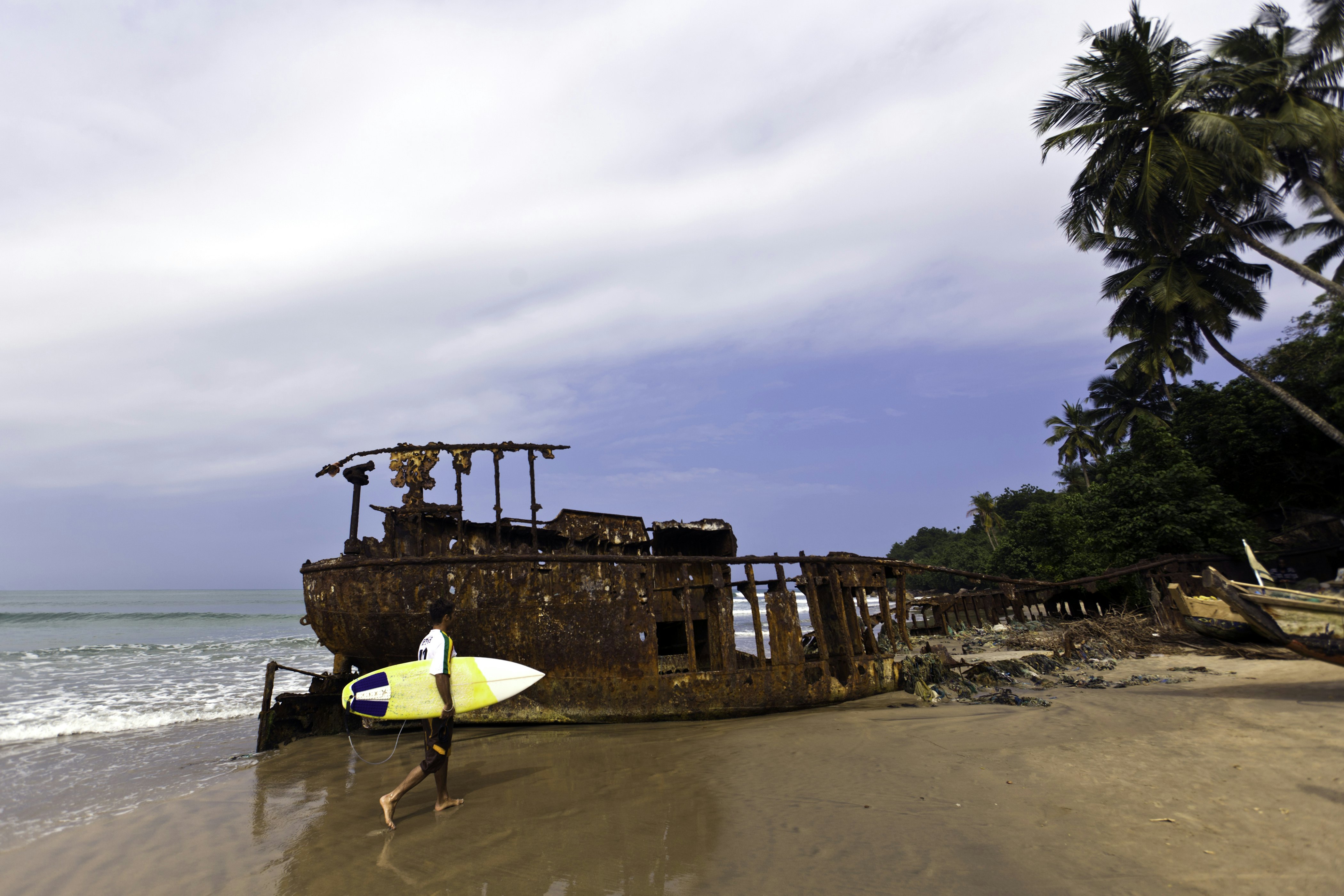 Surfer on beach near old shipwreck on the coast of Ghana