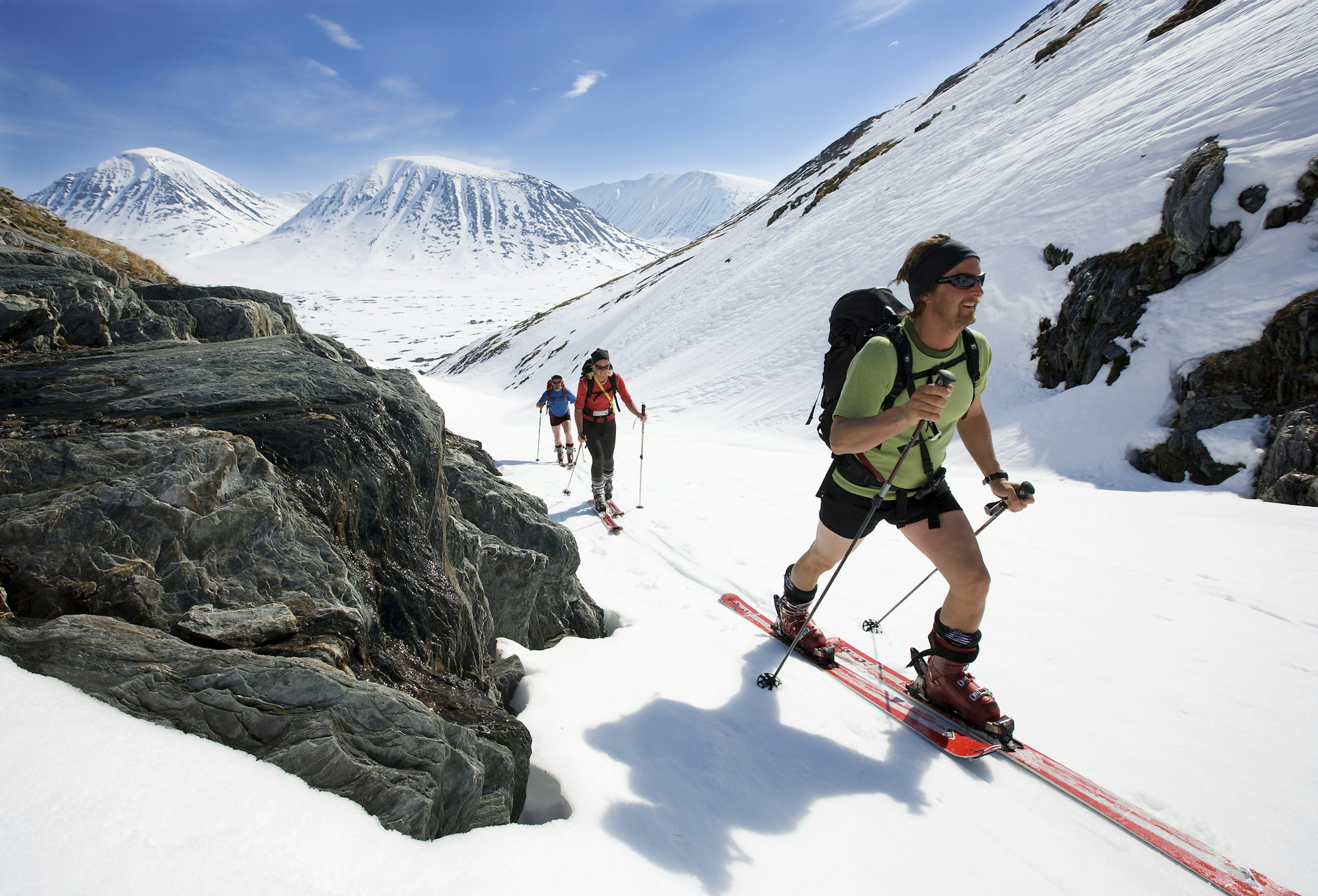 Three cross-country skiers move uphill as the sun shines down upon them.