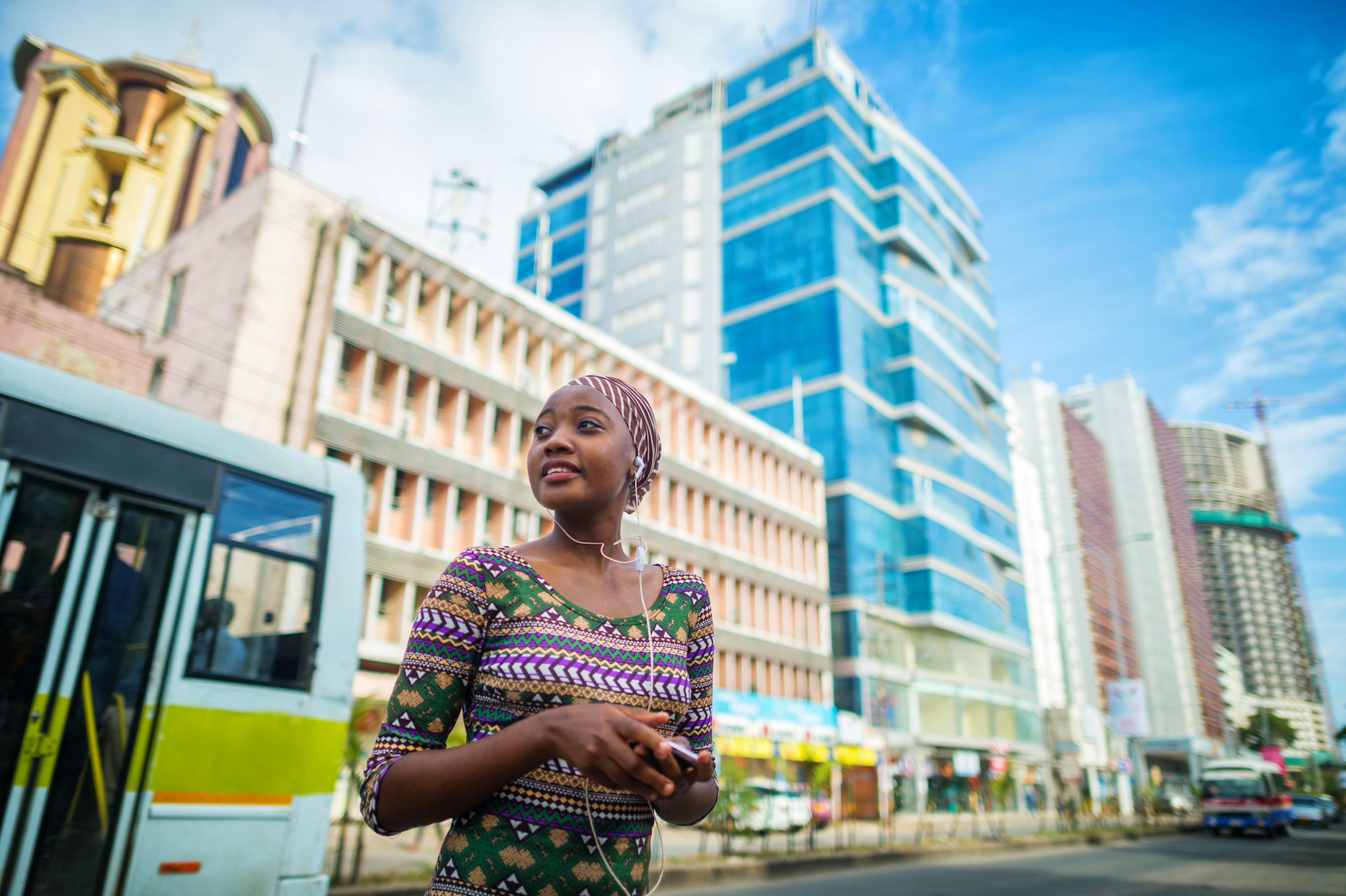 A young woman listening to music stands in street against modern buildings in the center of Dar-es-Salaam, Tanzania, East Africa