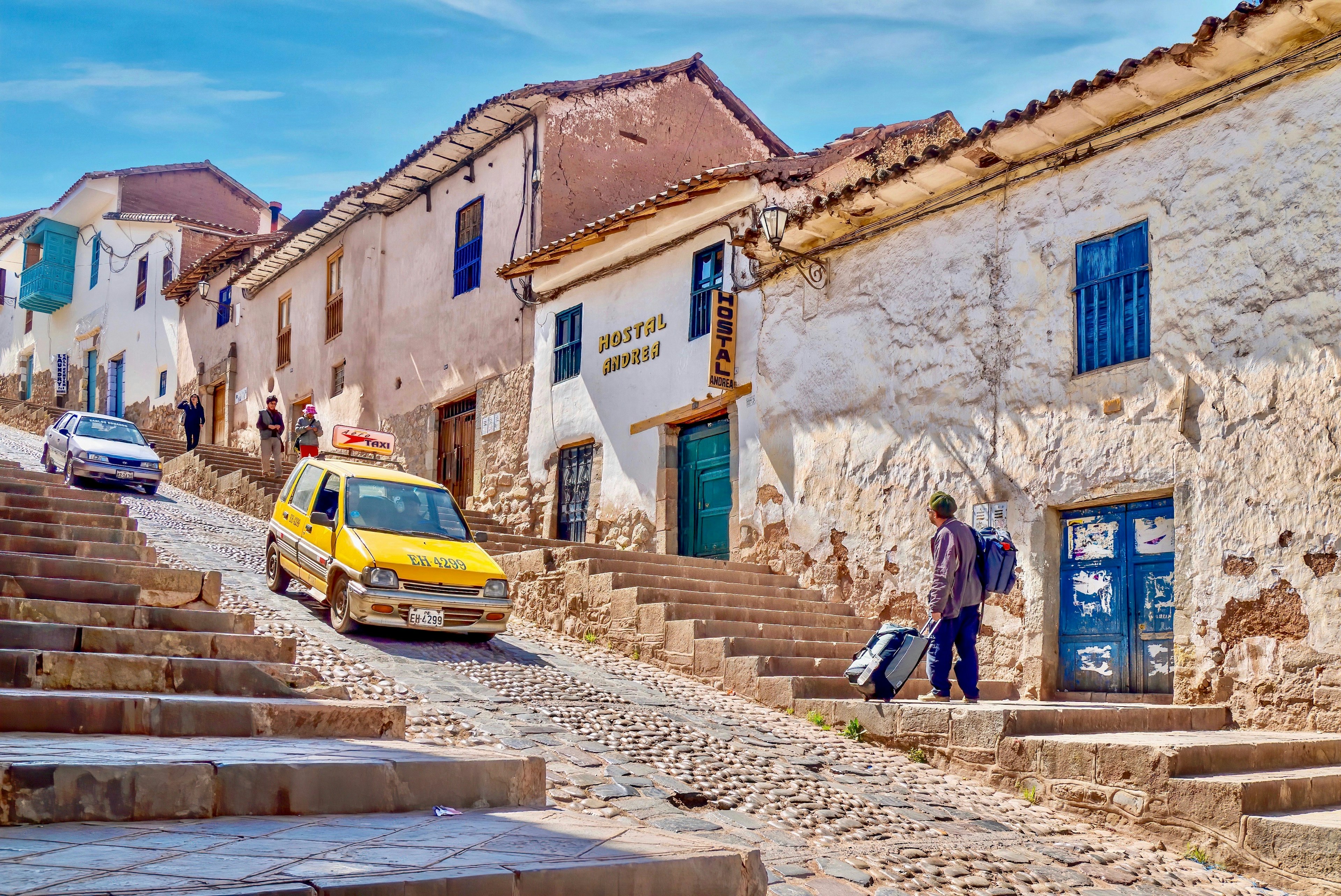 A taxi drives down a steep, cobbled street in the historic center of Cusco. The buildings lining the streets have been converted into quaint hotels.