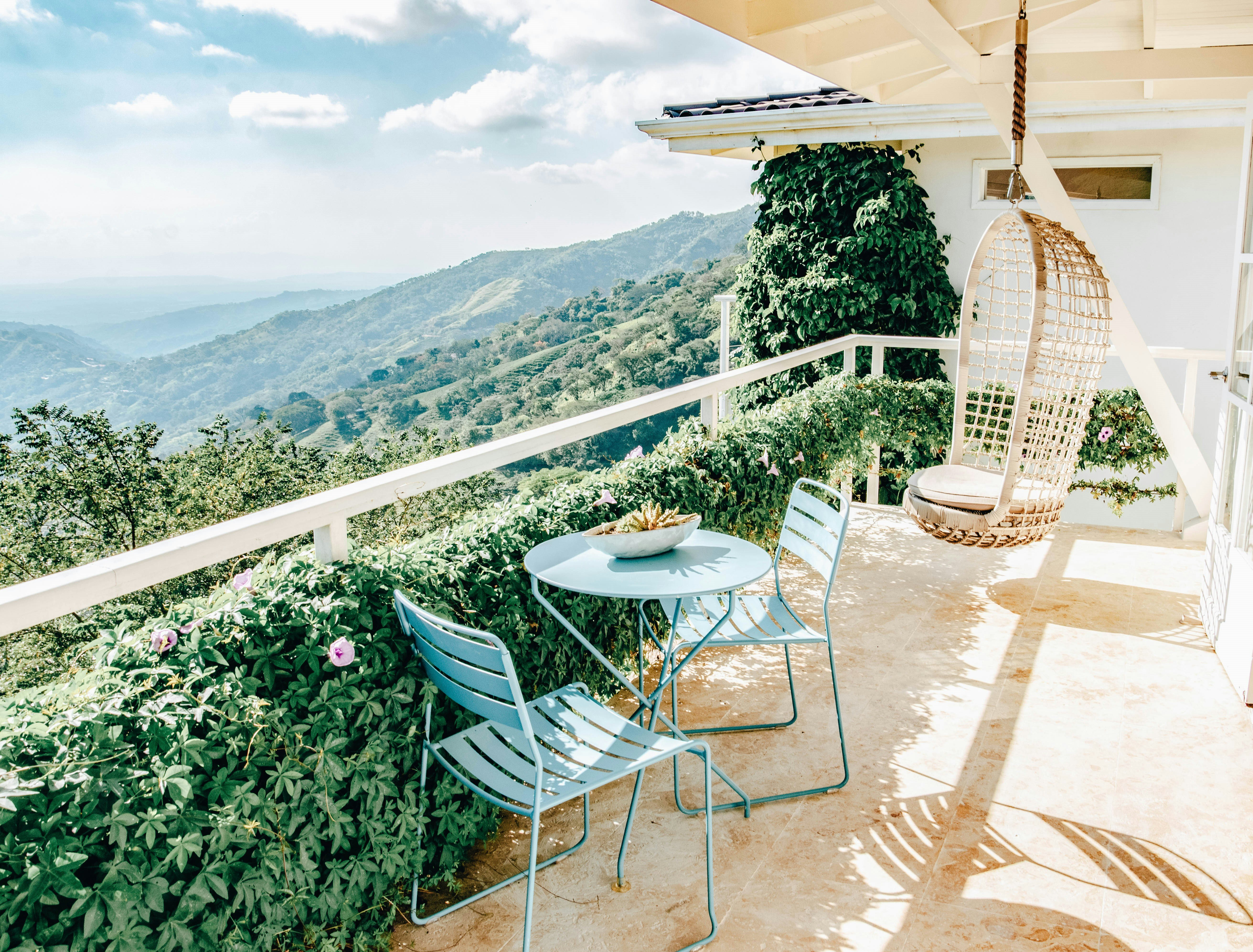 A terrace with a table and two chairs plus a swinging chair hanging from the ceiling. The view stretches out over lush hillsides and jungle