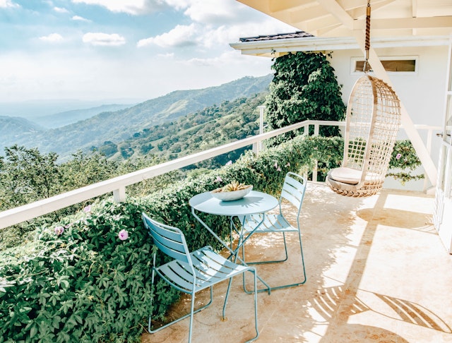 A terrace with a table and two chairs plus a swinging chair hanging from the ceiling. The view stretches out over lush hillsides and jungle