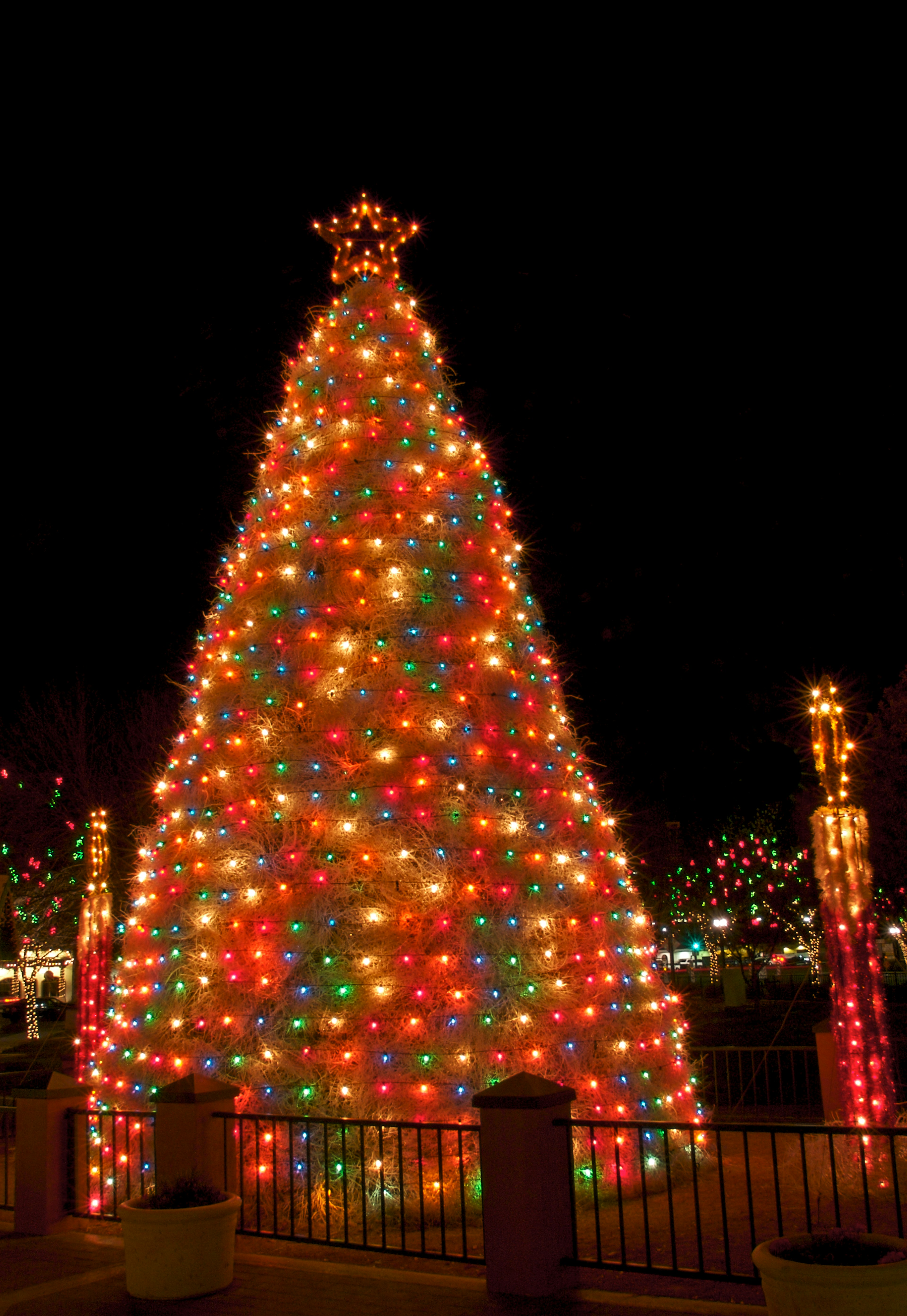 A tumbleweed Christmas tree covered in multi-colored Christmas lights shines at night