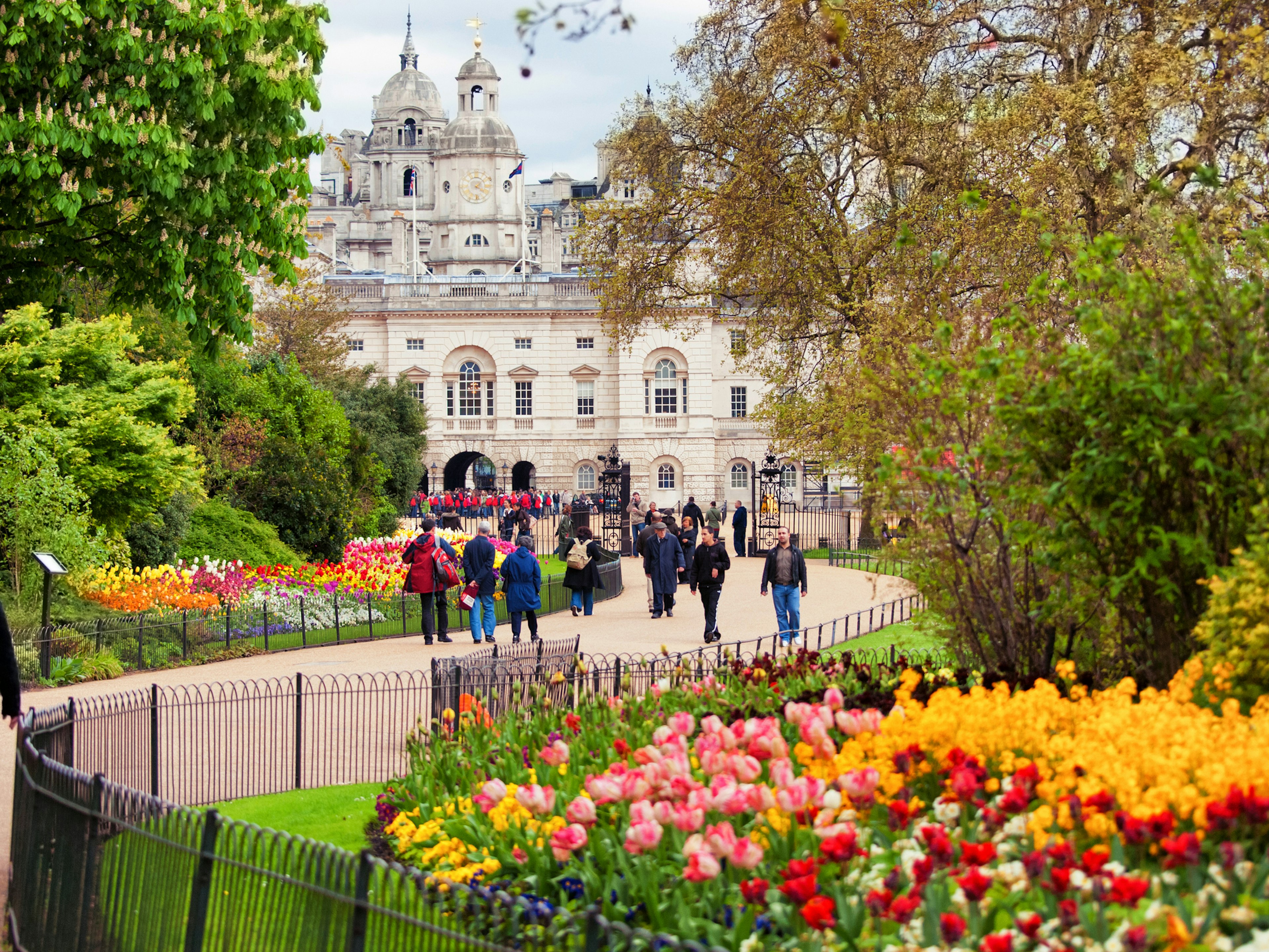 People walk along a path near a massive bed of bright orange, red and yellow tulips in London's St James' Park