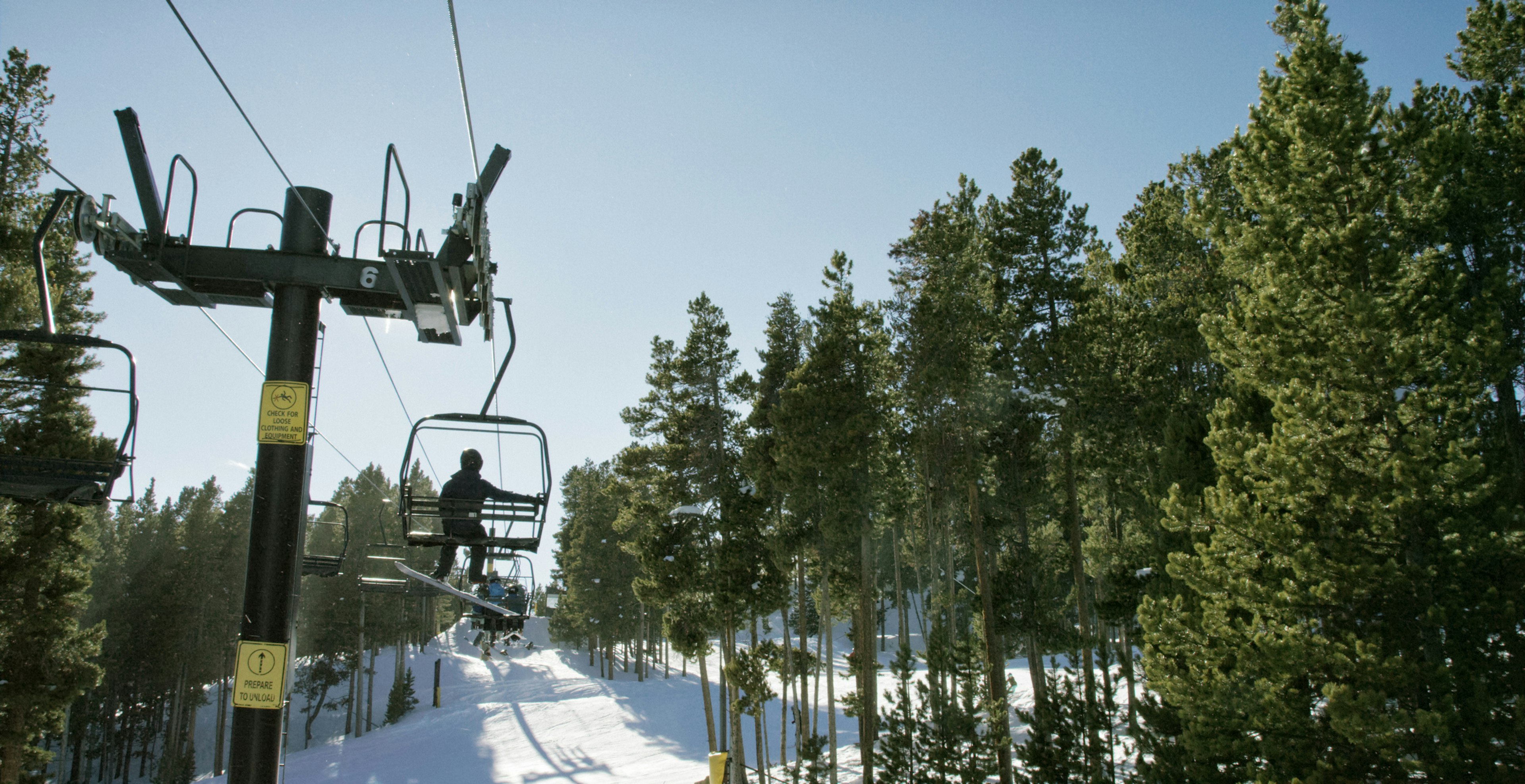 Snowboarders ride a ski lift on a bright, clear, sunny day