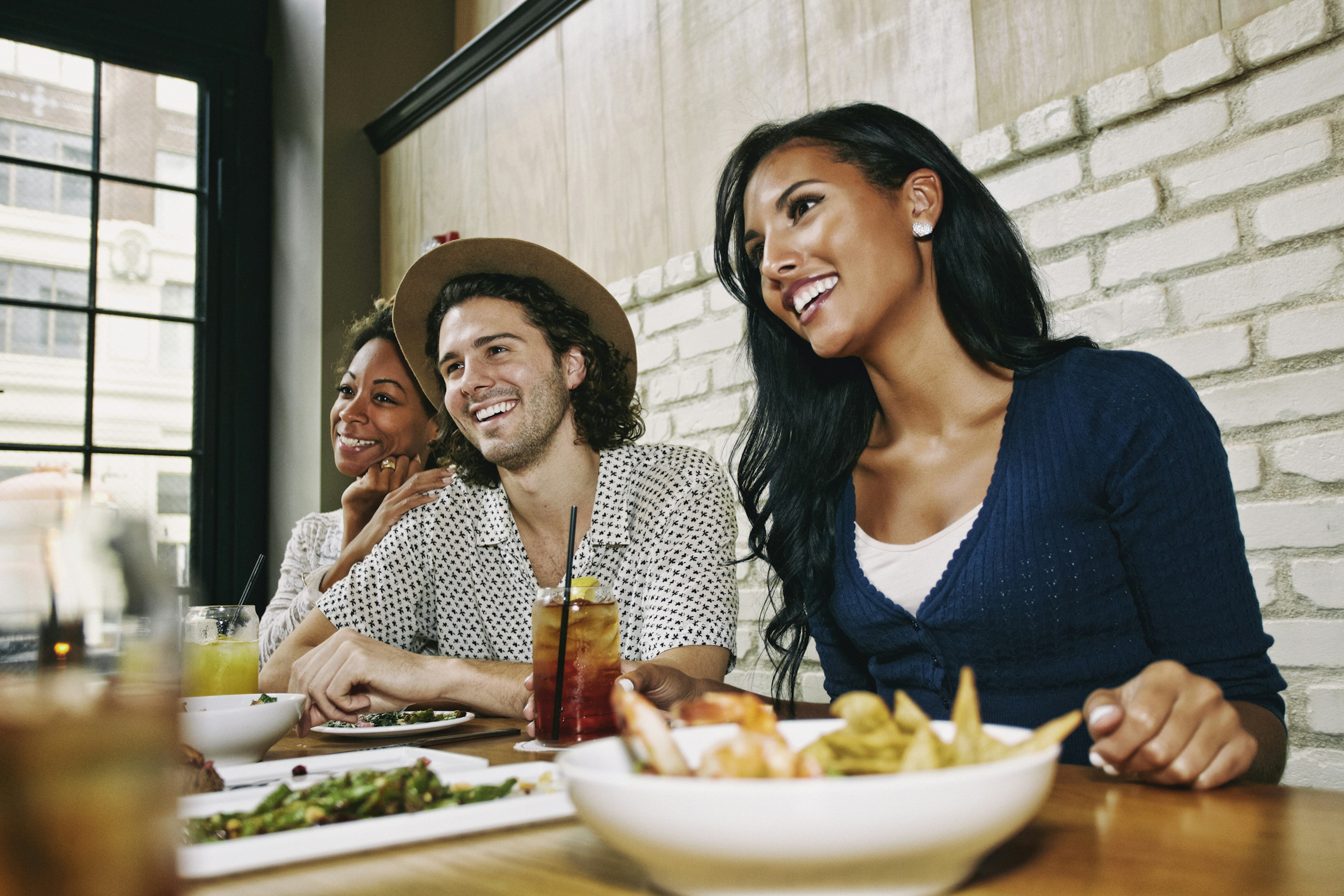 Smiling friends enjoying food and cocktails at table in bar