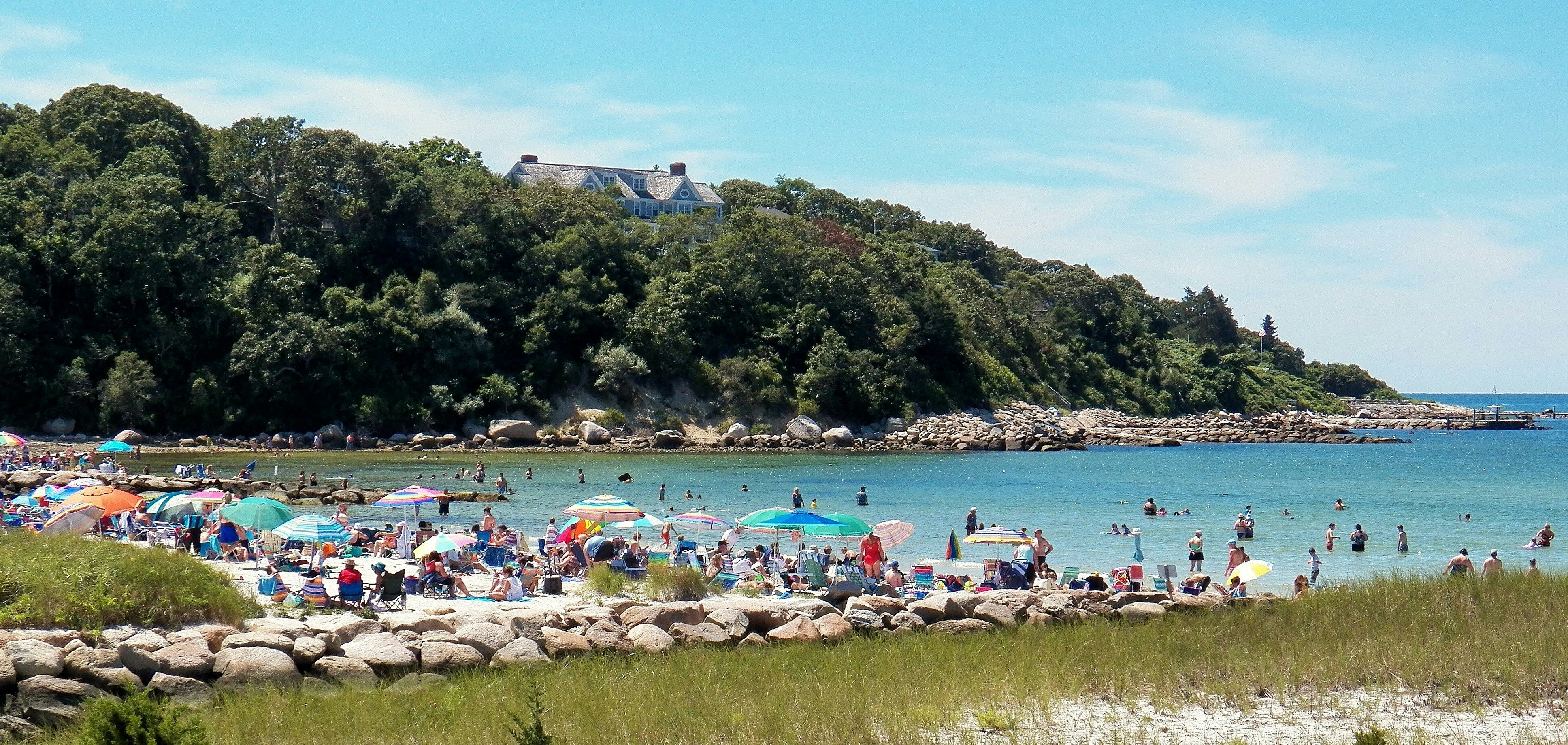 A view towards a beach lined with colorful sunshades as families vie for a spot