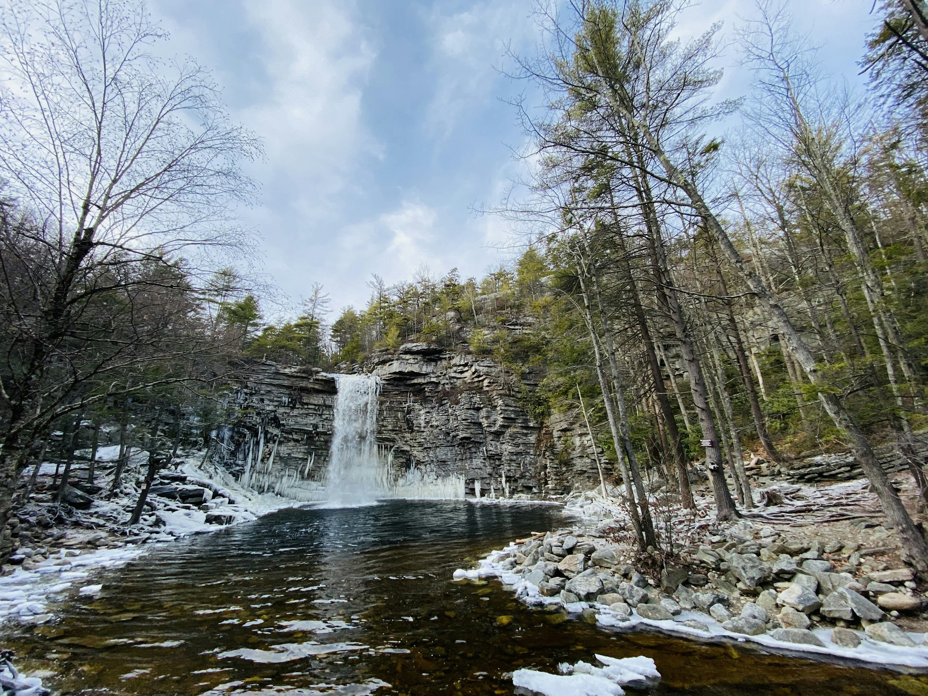 A waterfall plunges down into an icy pond surrounded by snow