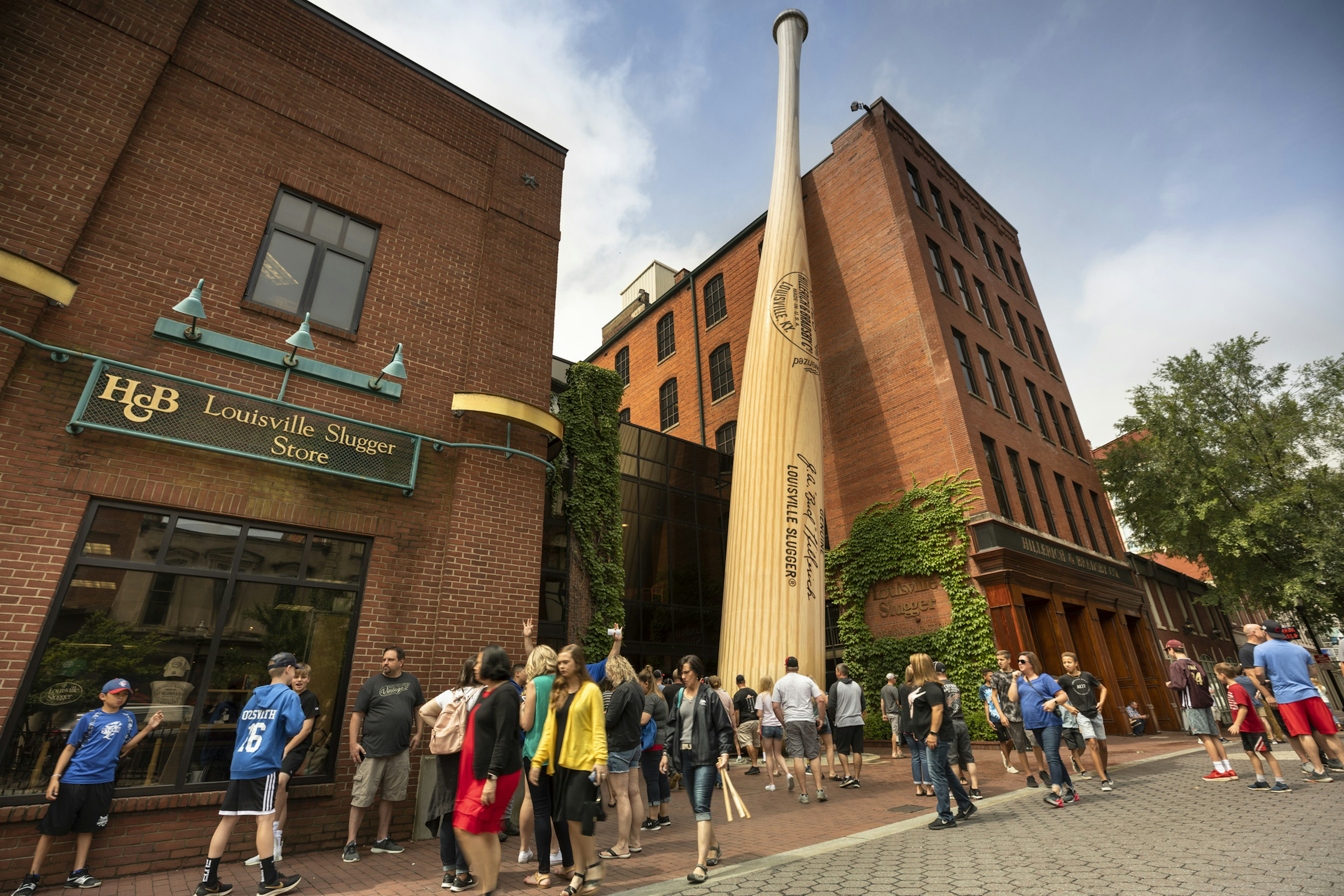 A red-brick museum in Louisville with a huge baseball bat outside it and tourists milling around nearby