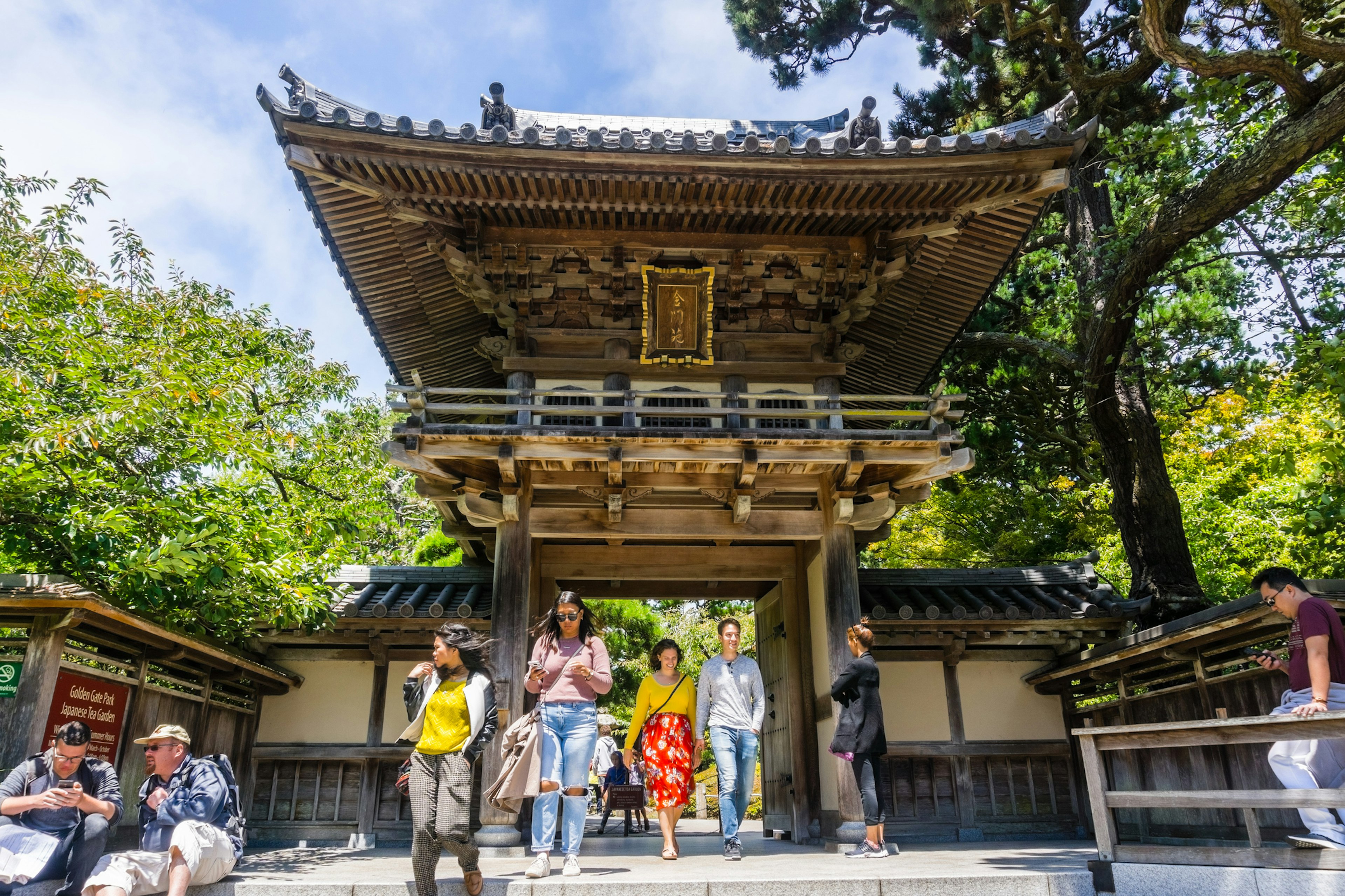 A wooden gateway marks the entrance to a Japanese Tea Garden. Tourists are milling around out front