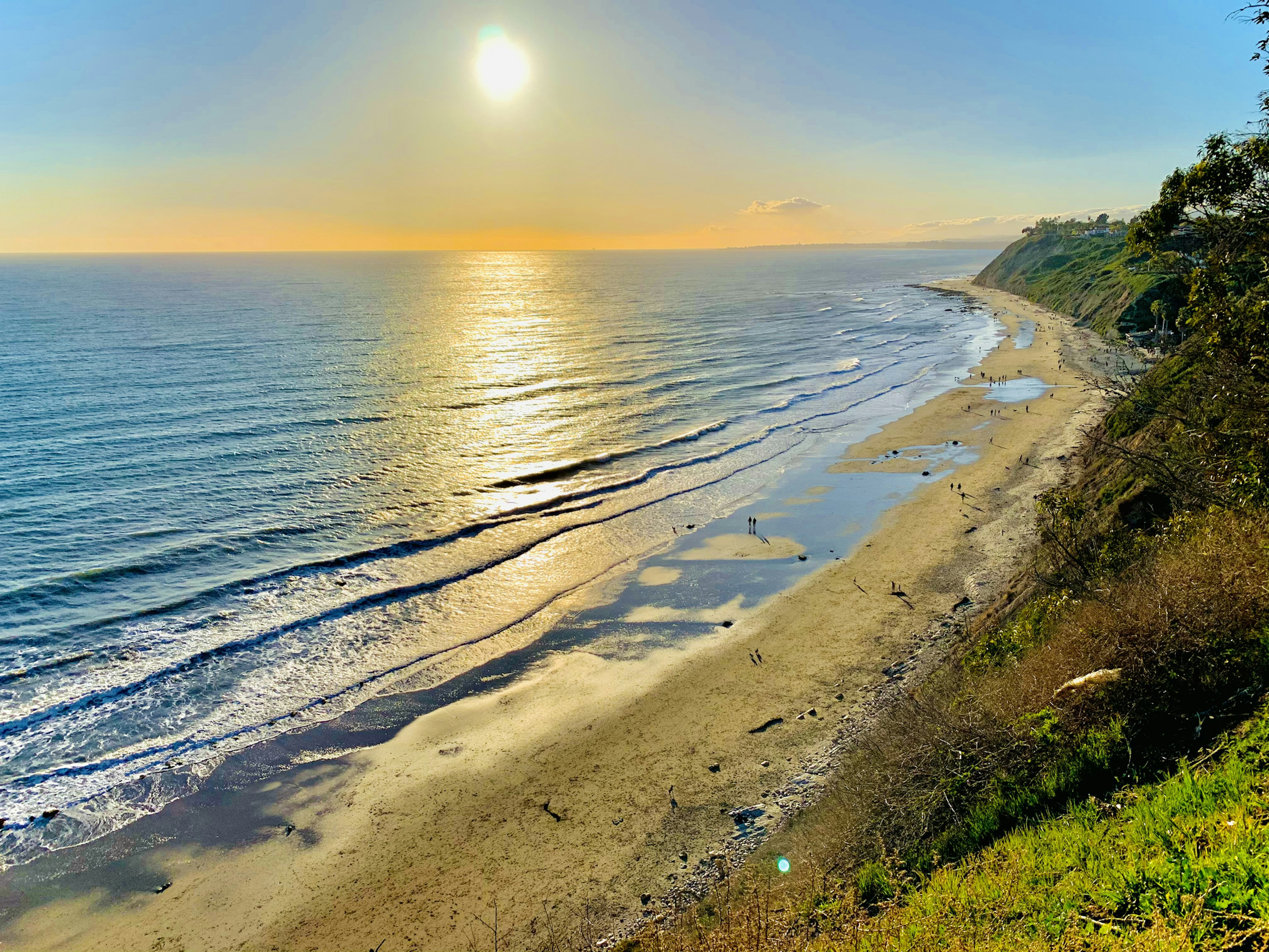 Looking down from a clifftop towards a beach with golden sand and several groups of people walking along it