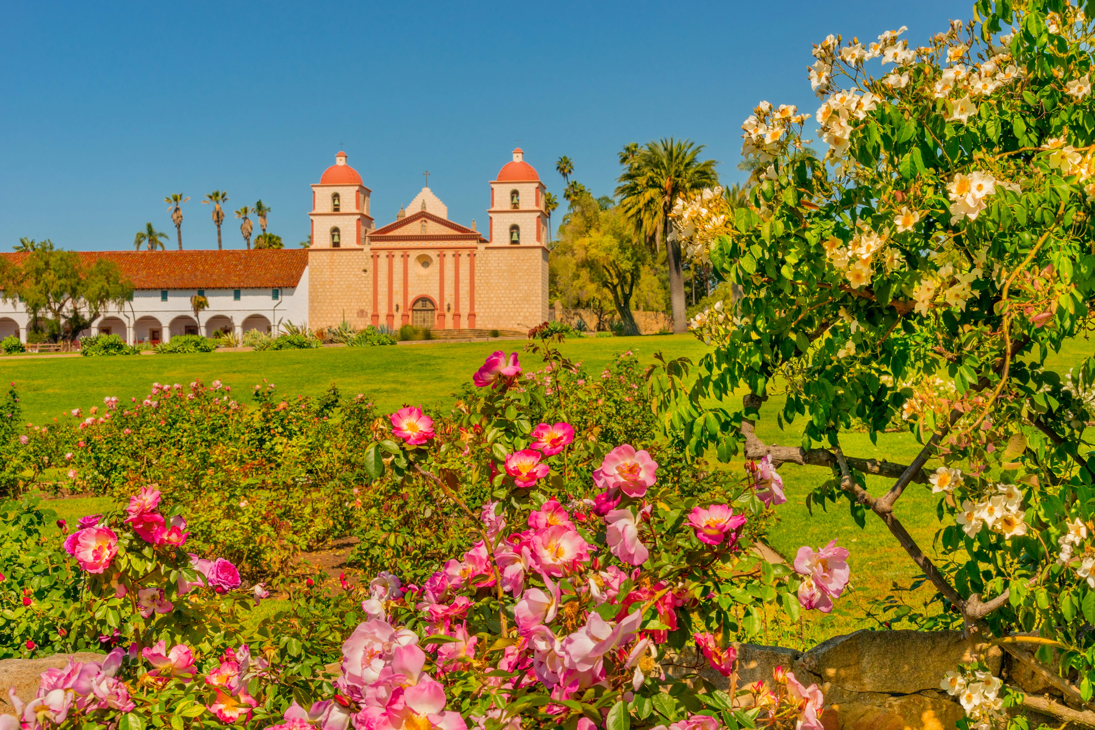 Flowers in bloom in pinks and yellows in the garden of a Spanish-style church building