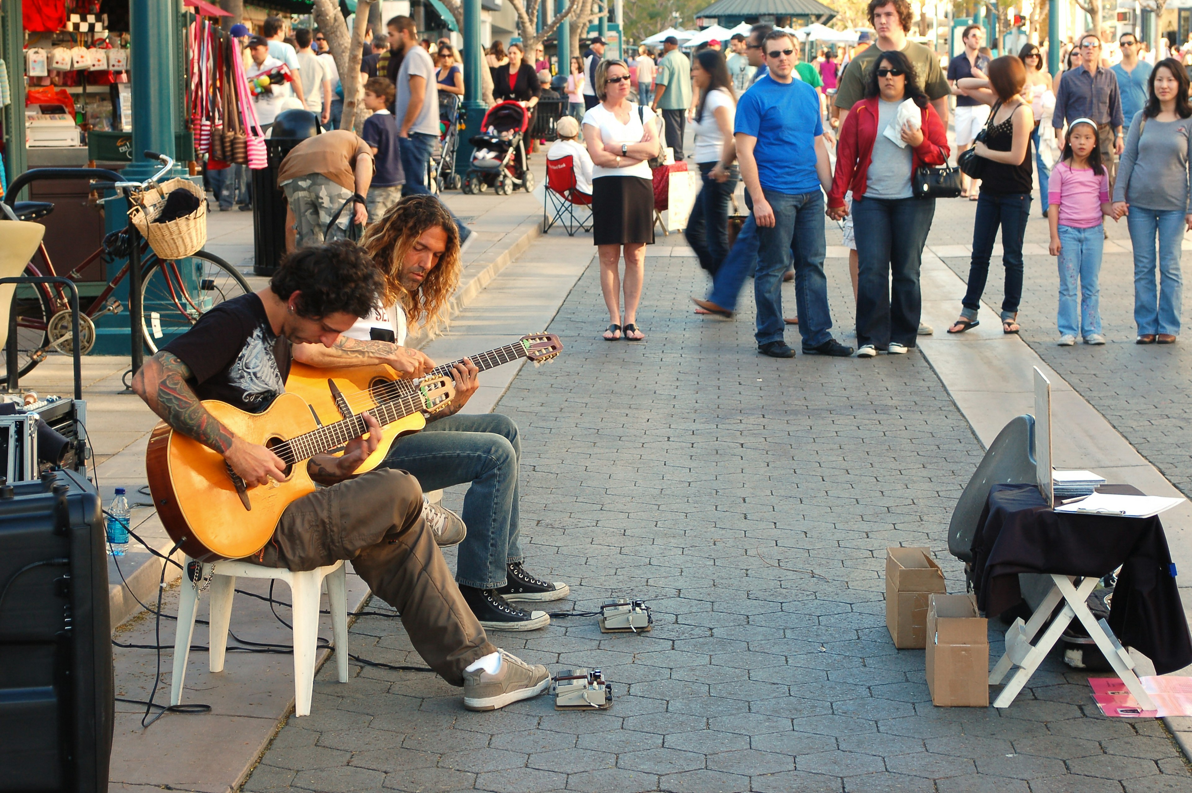 Two guitarists busk in a pedestrianized zone with plenty of onlookers