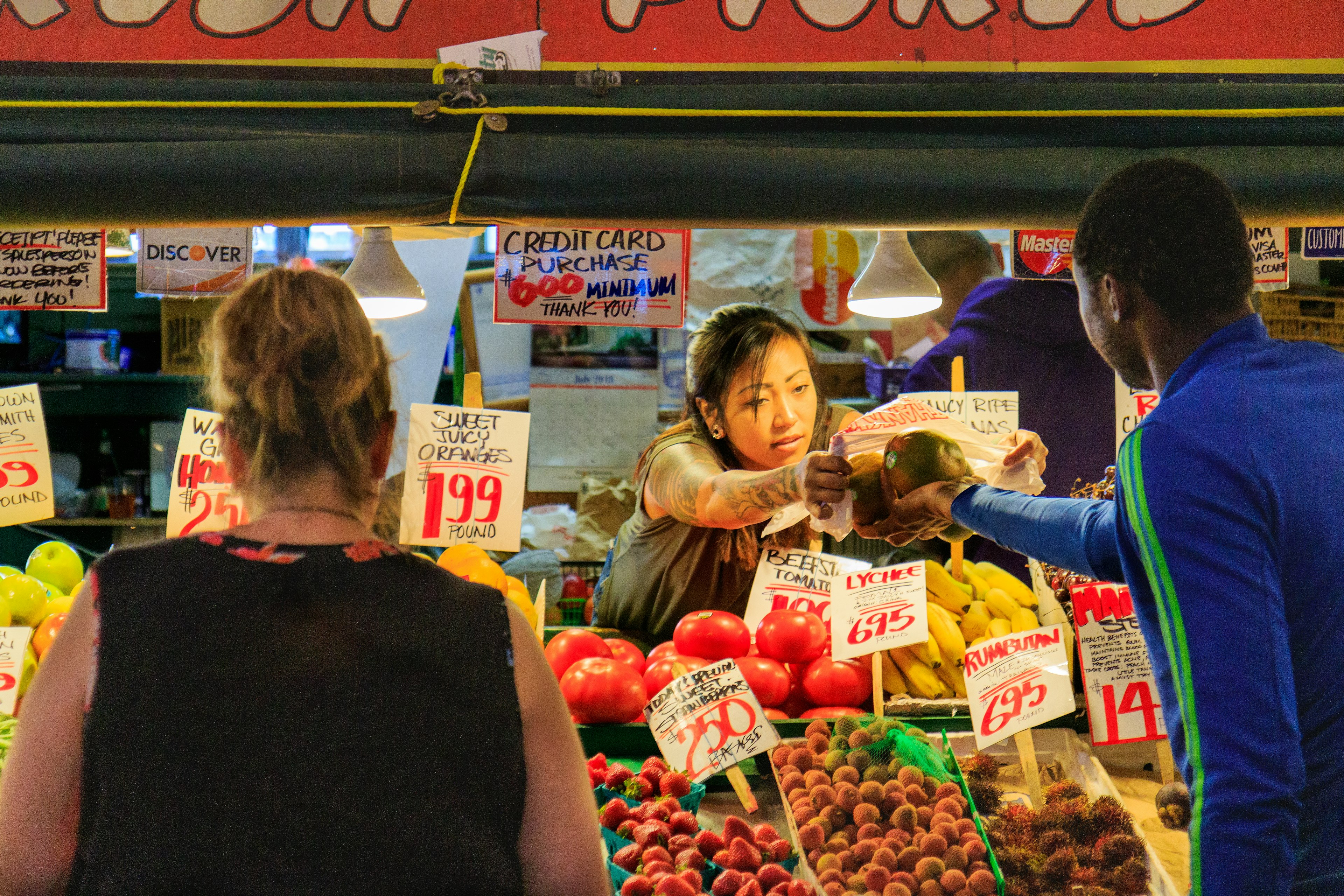 A woman working at a market stall hands produce over to a customer