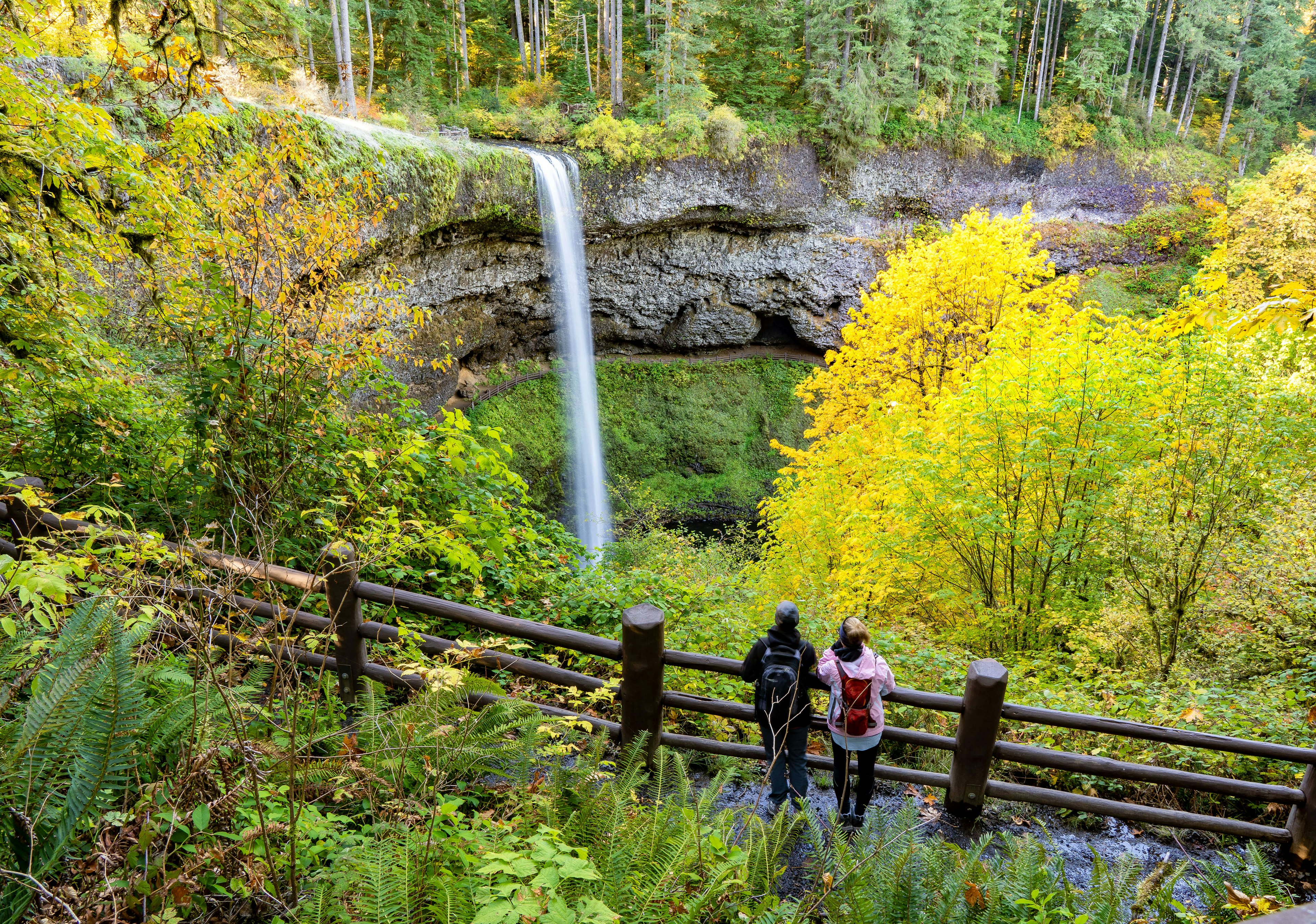 Two women looking at South falls and trees in autumn season showing fall colors, in Silver Falls State Park near Silverton, Oregon