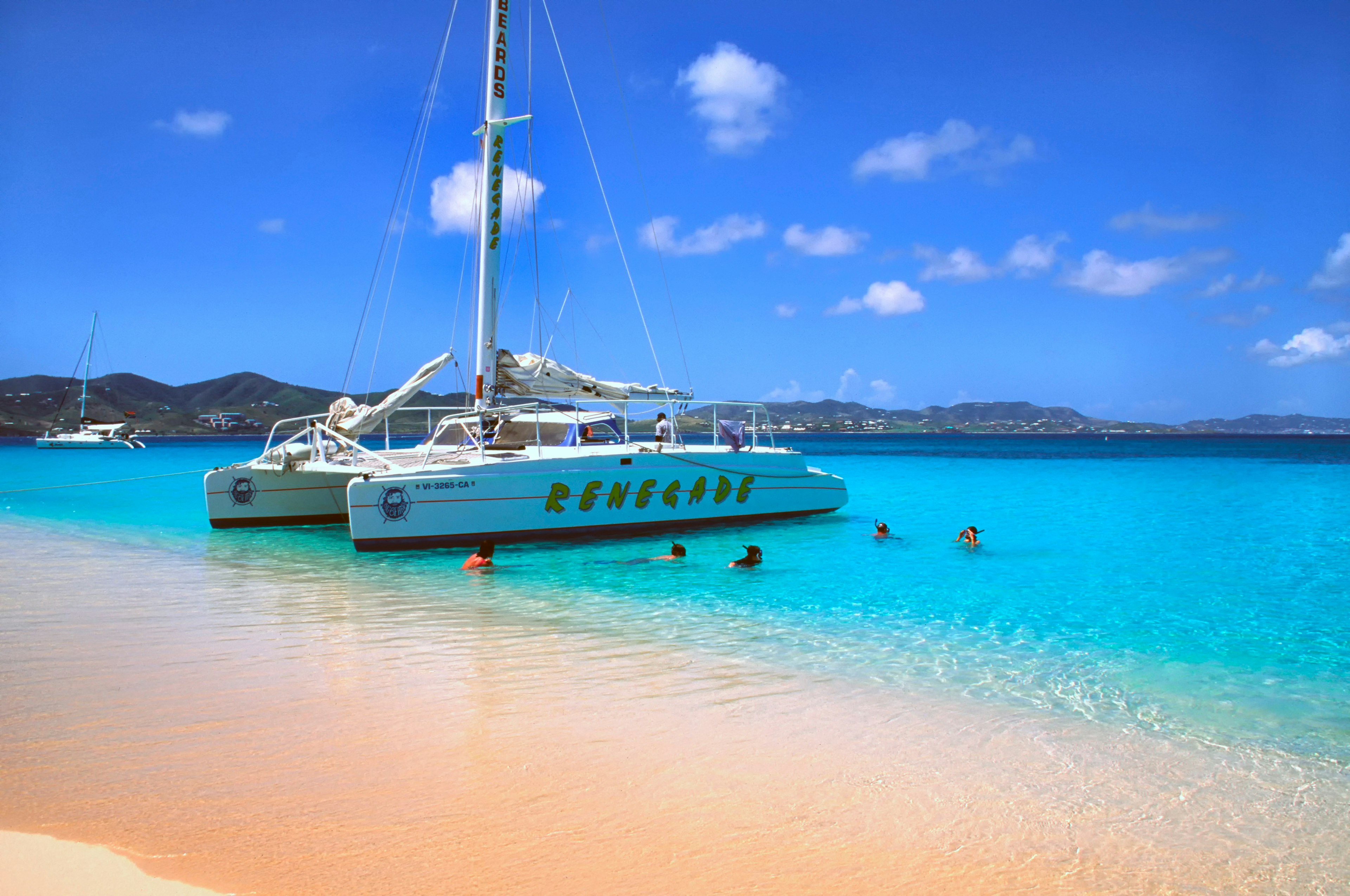 People snorkel the blue waters next to a catamaran by the sands of Buck Island National Park, St Croix, US Virgin Islands, USA