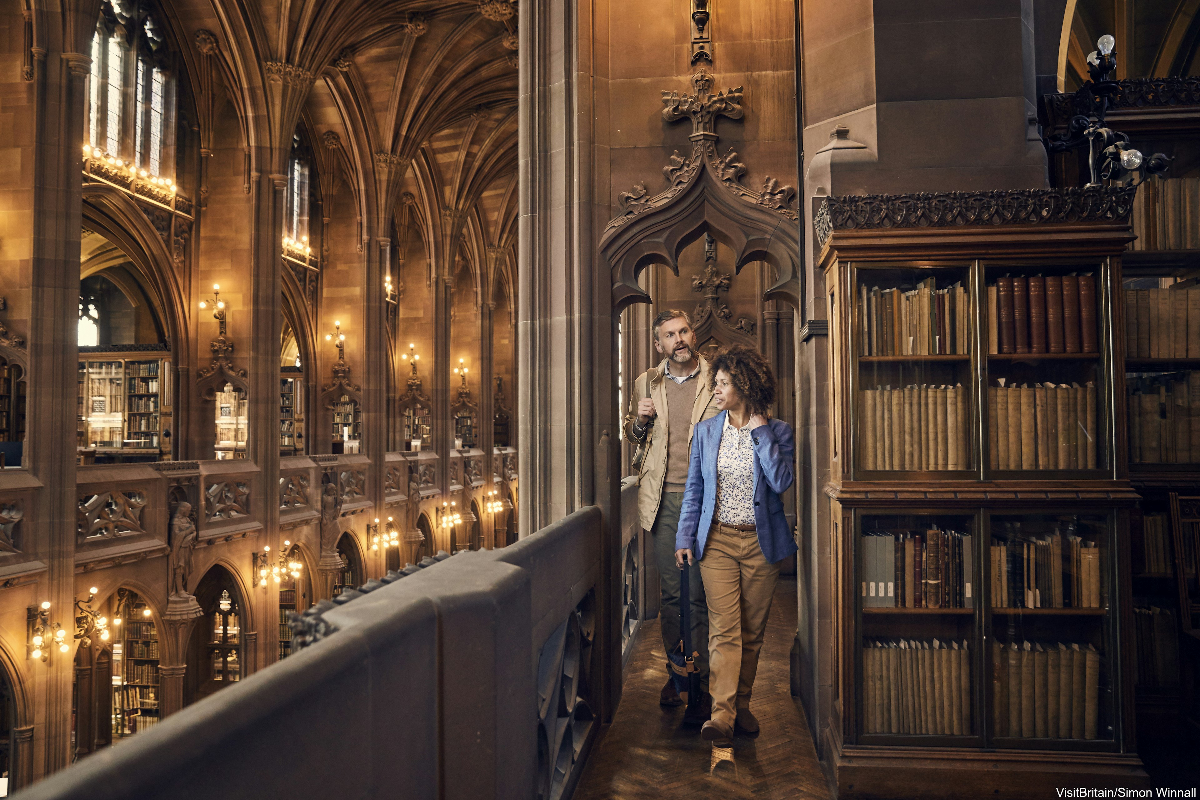 A couple walking along the balconies past book stacks in the galleries in the historic Reading Room in John Rylands Library, part of the University of Manchester.