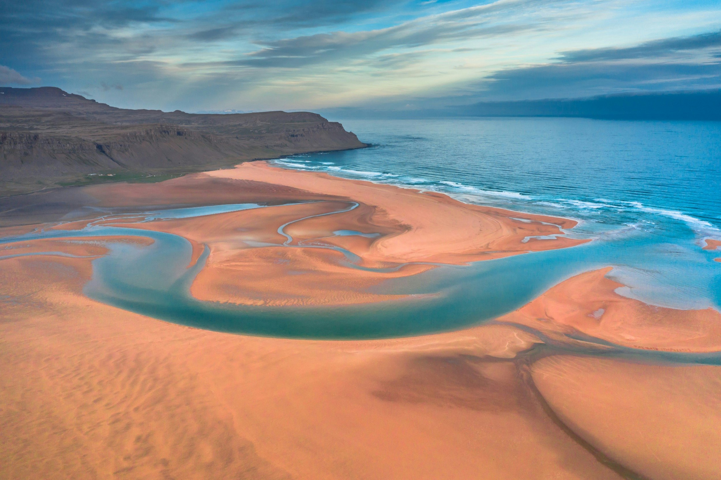 A vast sandy beach in oranges and golds with azure water flowing through channels in the sand