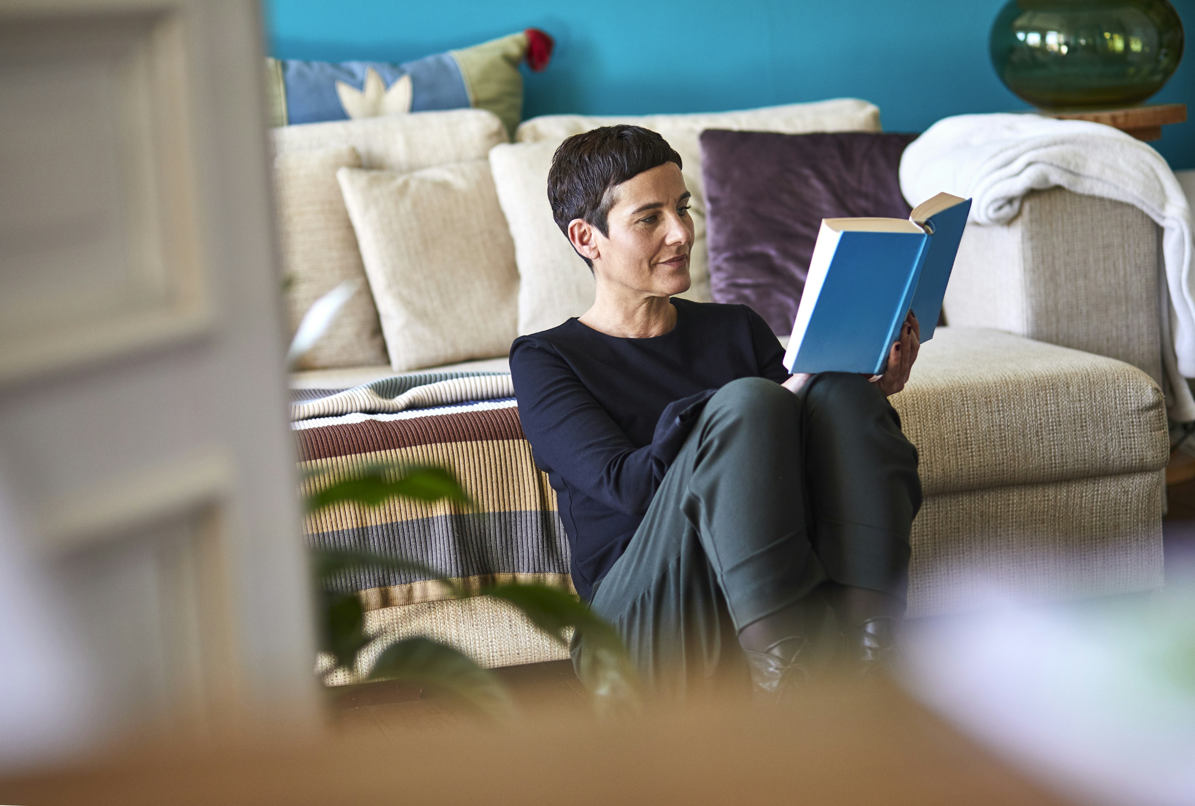 Woman reading book sitting on the floor at home