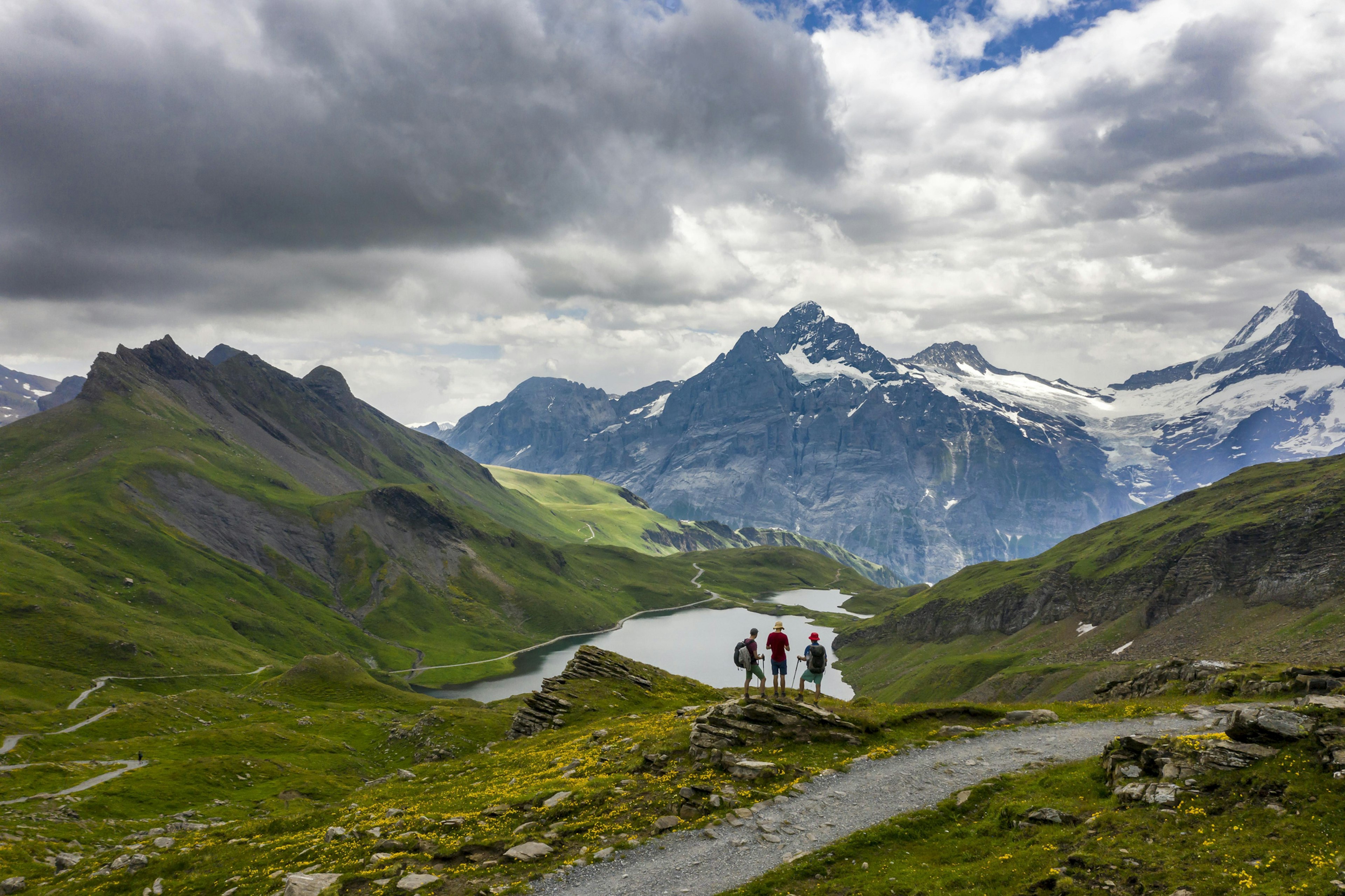 Three hikers stand together gazing down upon a lake in the mountains