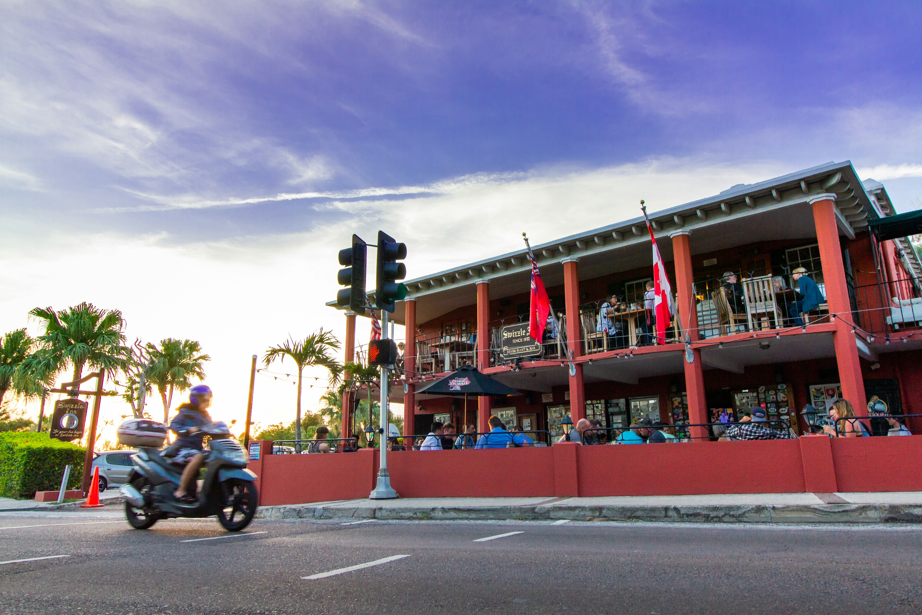 The Swizzle Inn Pub and Restaurant in Bermuda, a roadside pub with people sat at tables on the balcony and at ground-level