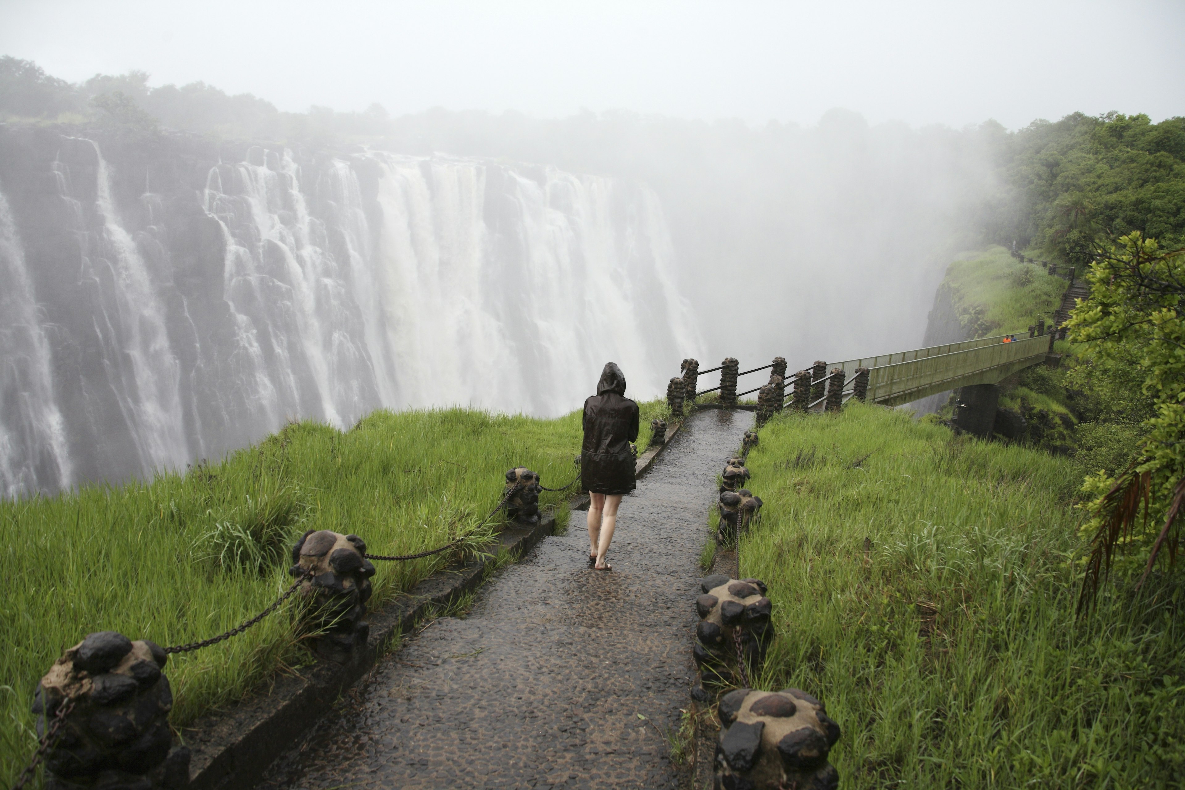 Woman walking towards foot bridge at Victoria Falls or Mosi-oa-Tunya (the Smoke that thunders), Victoria Falls, Livingstone, Zambia