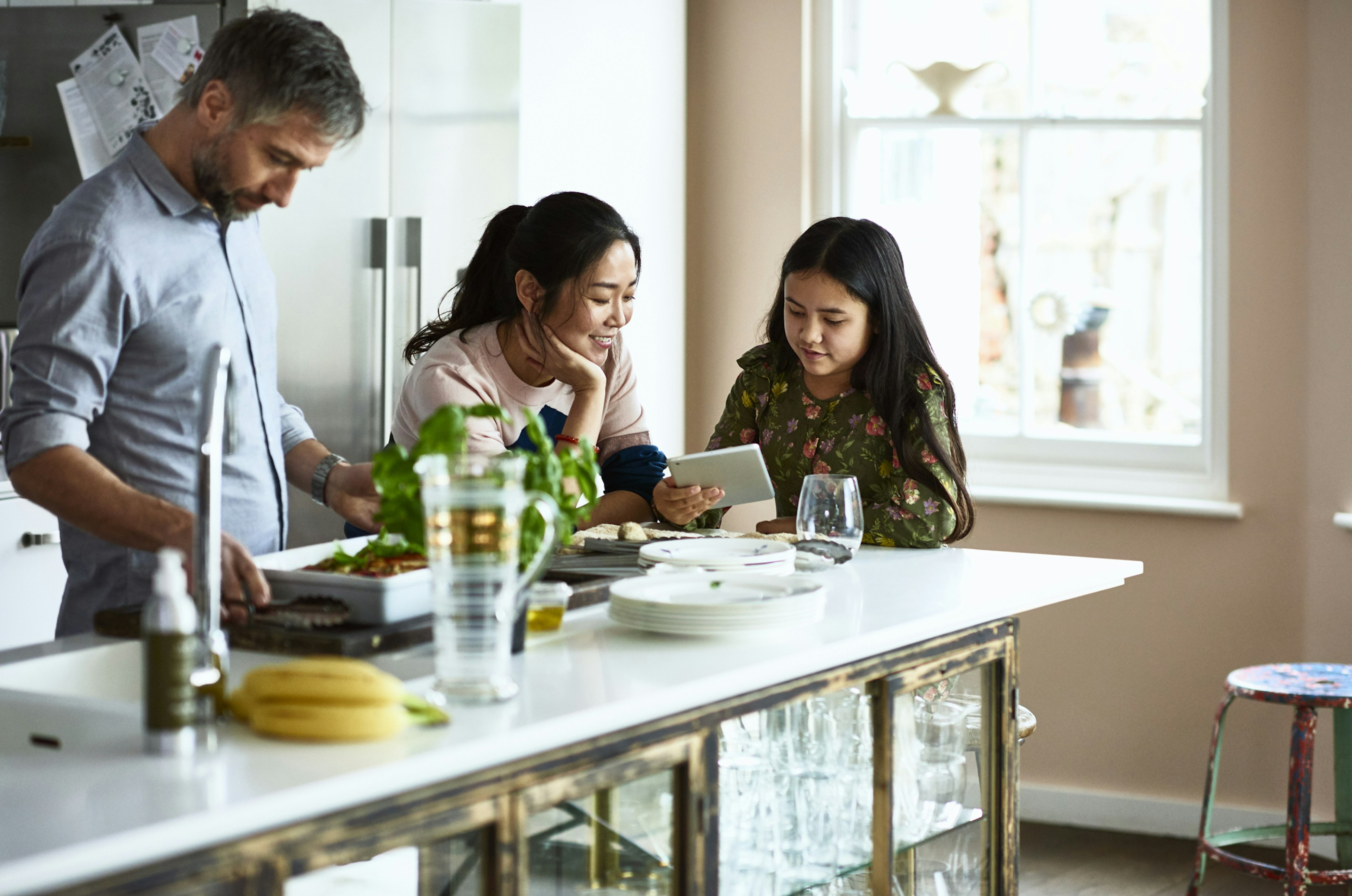 Mother and daughter looking at tablet while father prepares home made meal