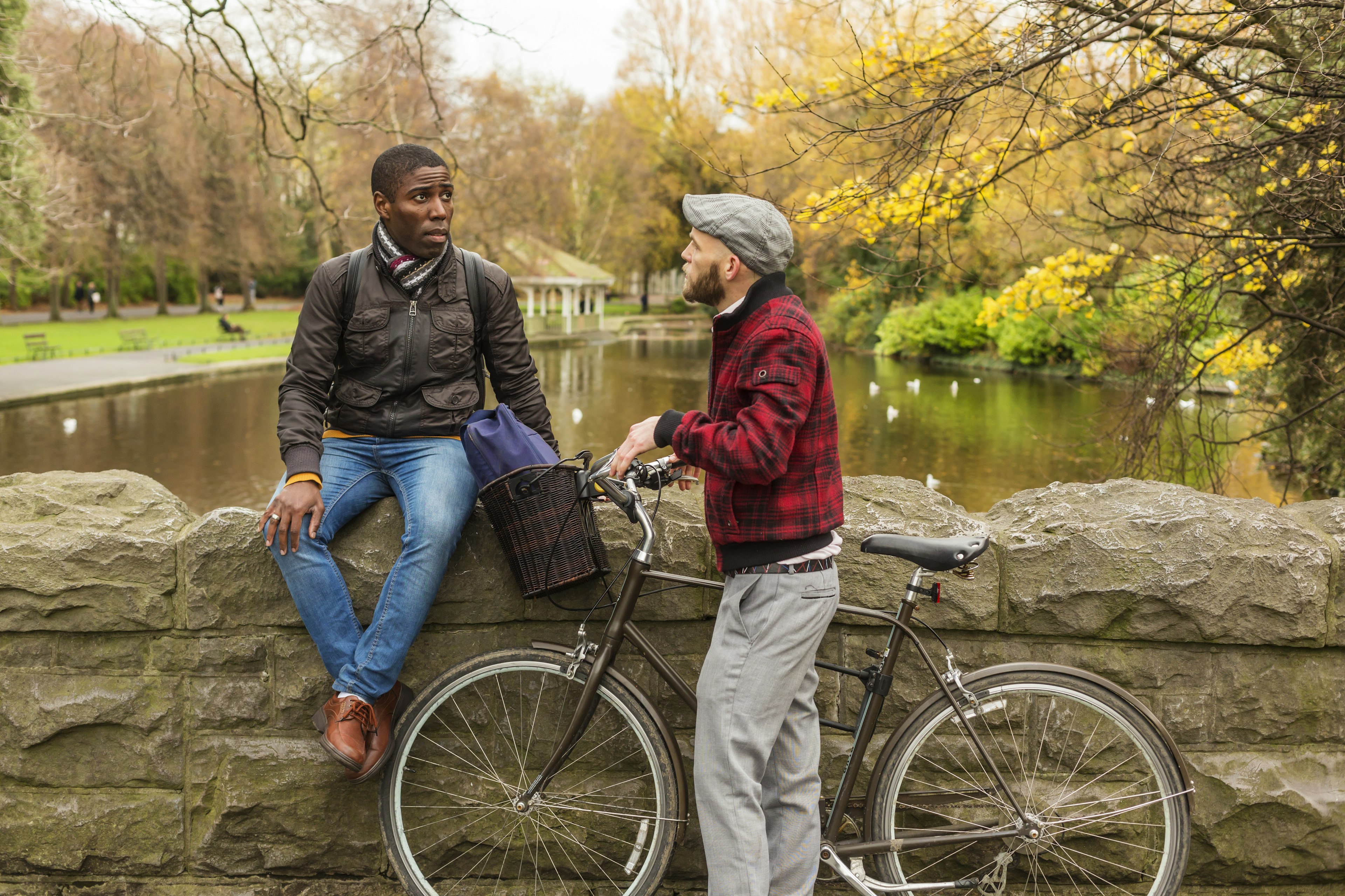 A man sits on stone wall talking to another man with a bicycle in a green park in Dublin, Ireland