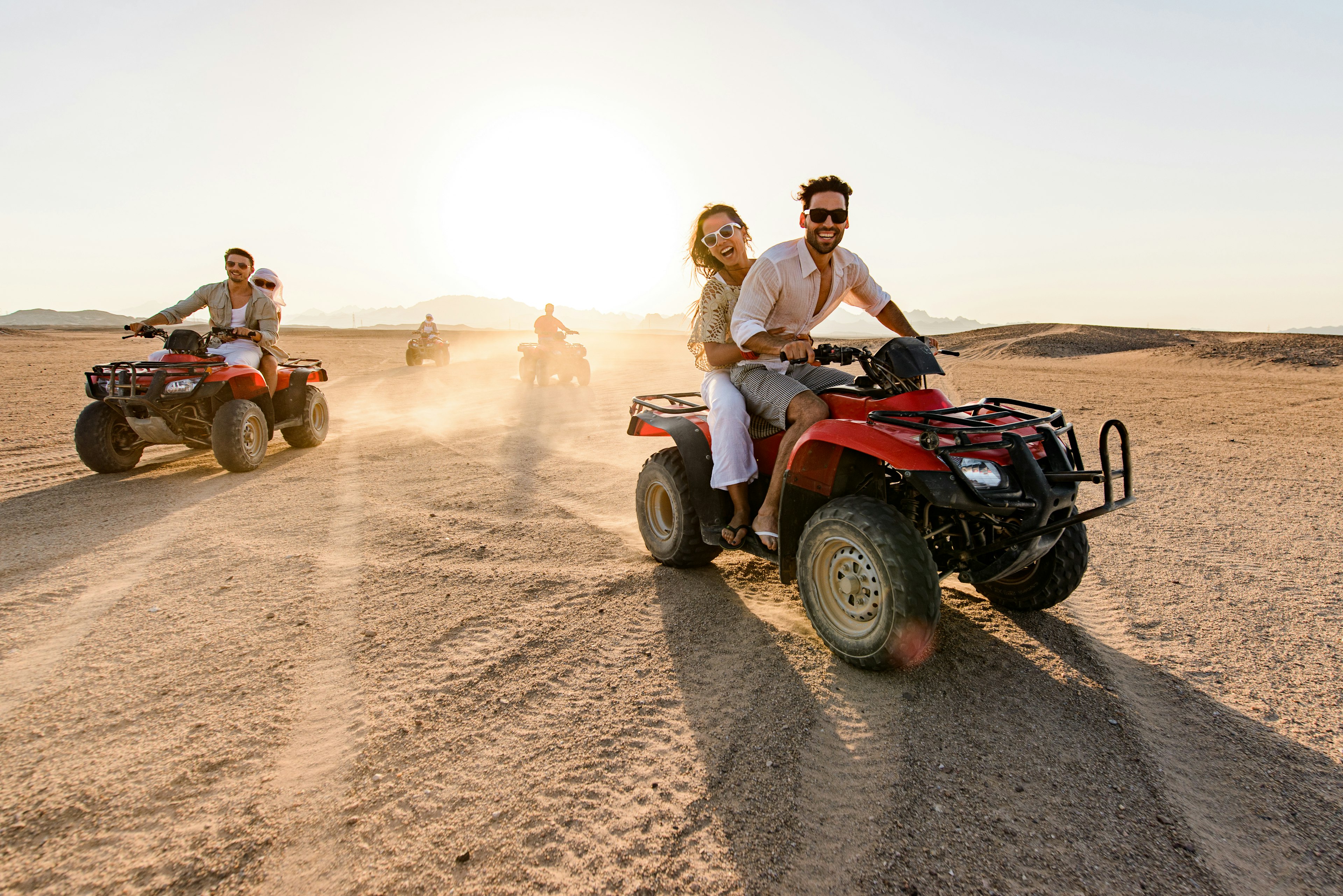 Group of friends having fun while driving quads in summer at the desert