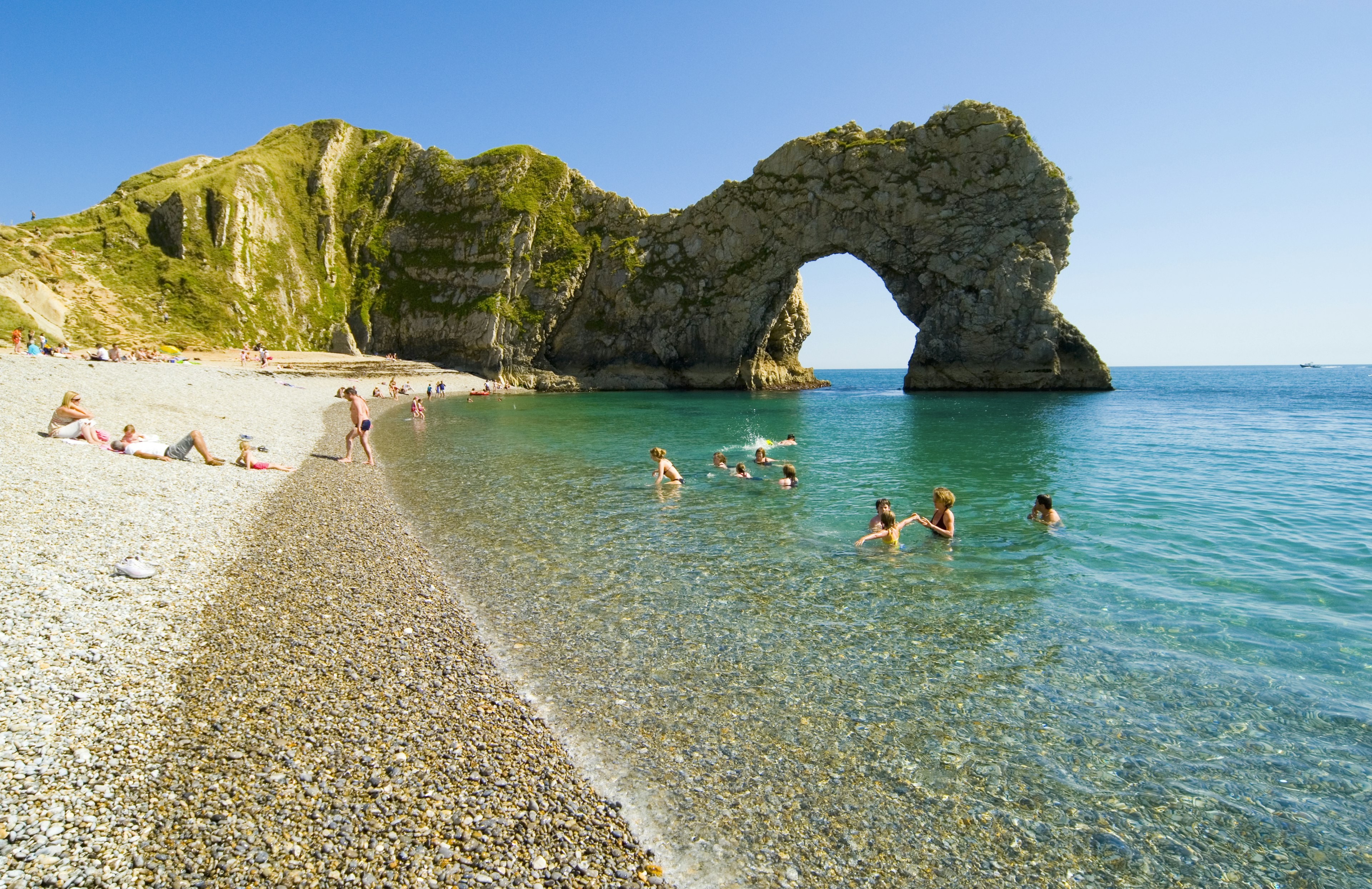 Children swim on a beach in front of Durdle Door, Jurassic Coast, Dorset, England, United Kingdom