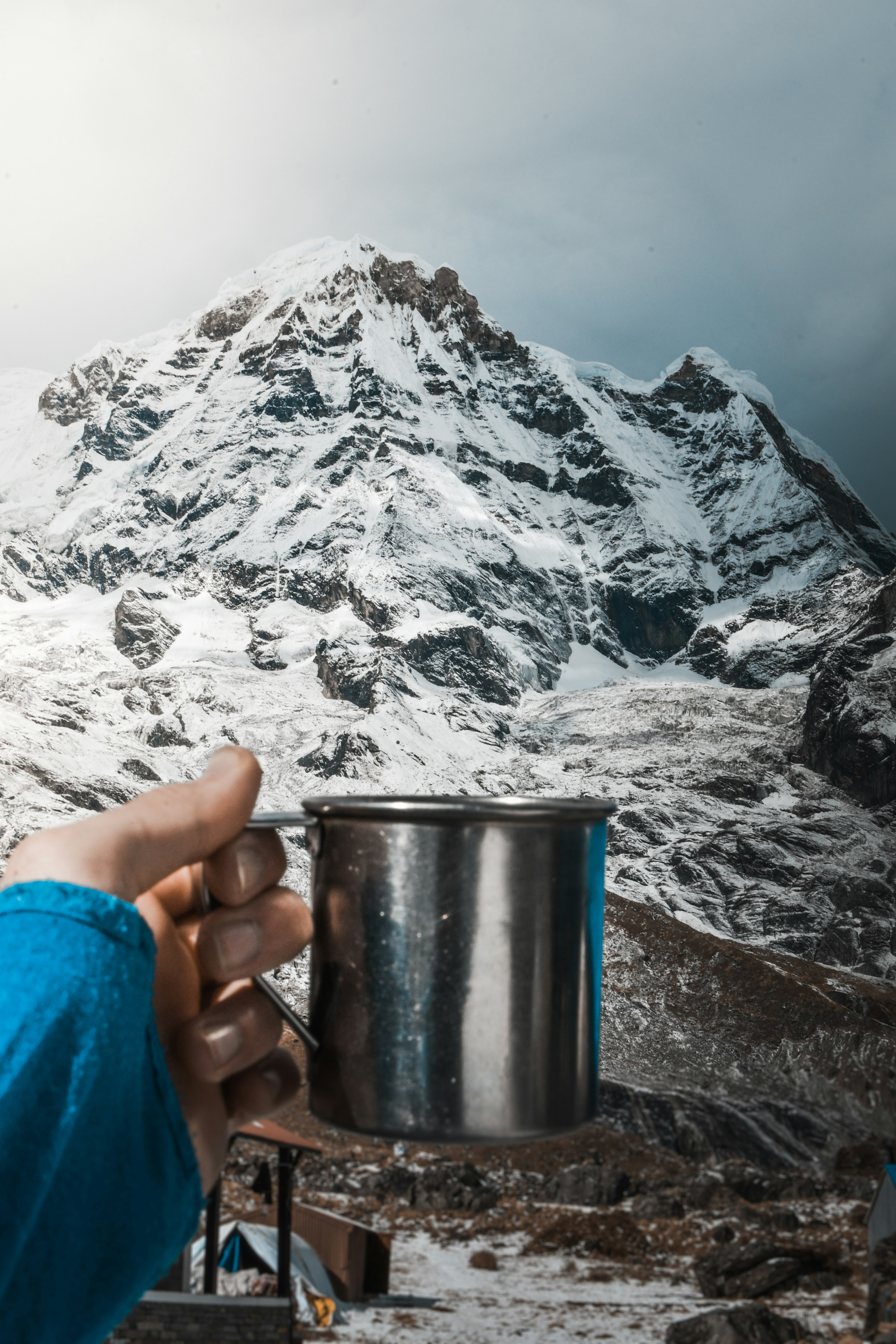 A close up of a metal mug of coffee in front of a mountain at base camp