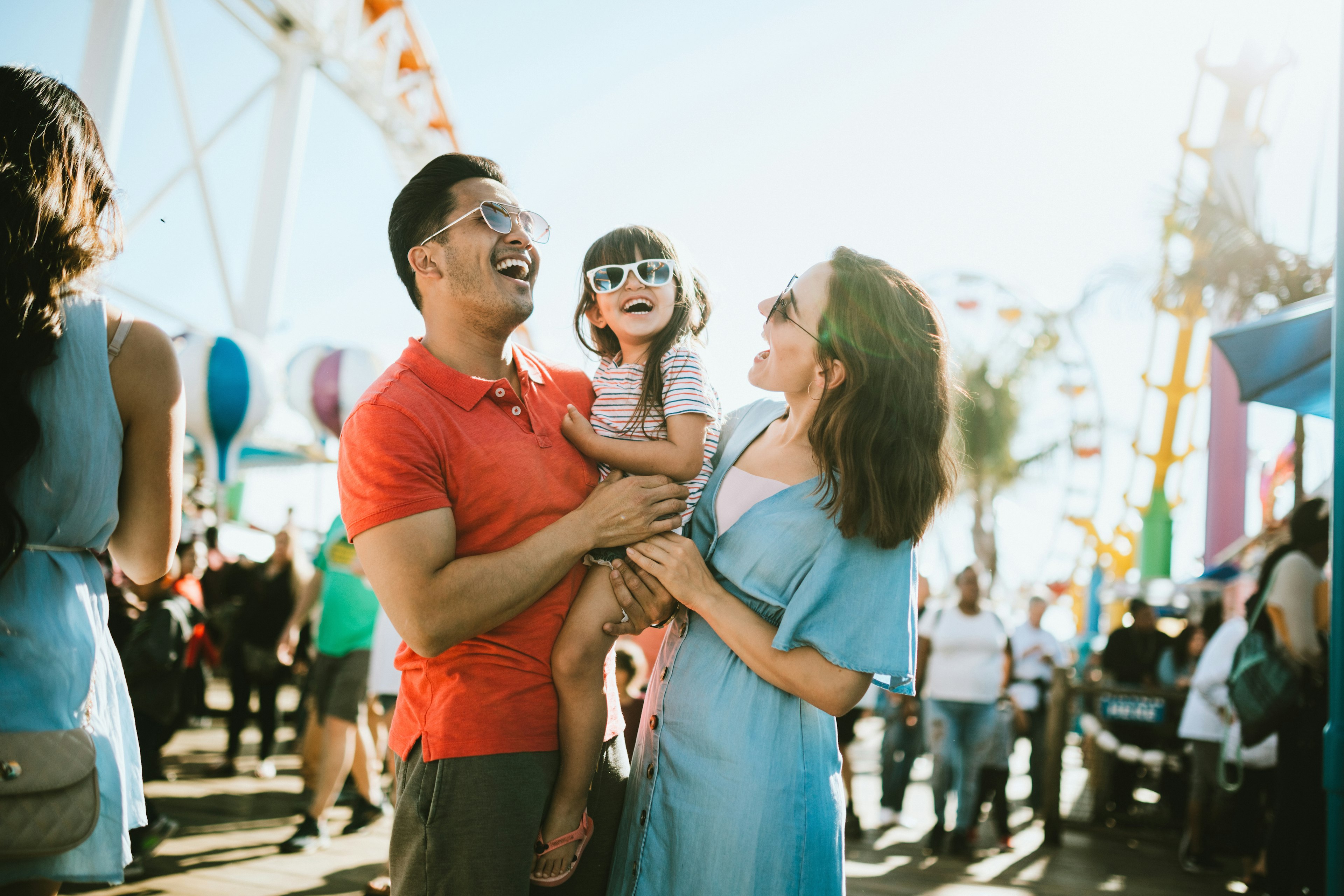 Parents stand either side of a child laughing at a fun fair