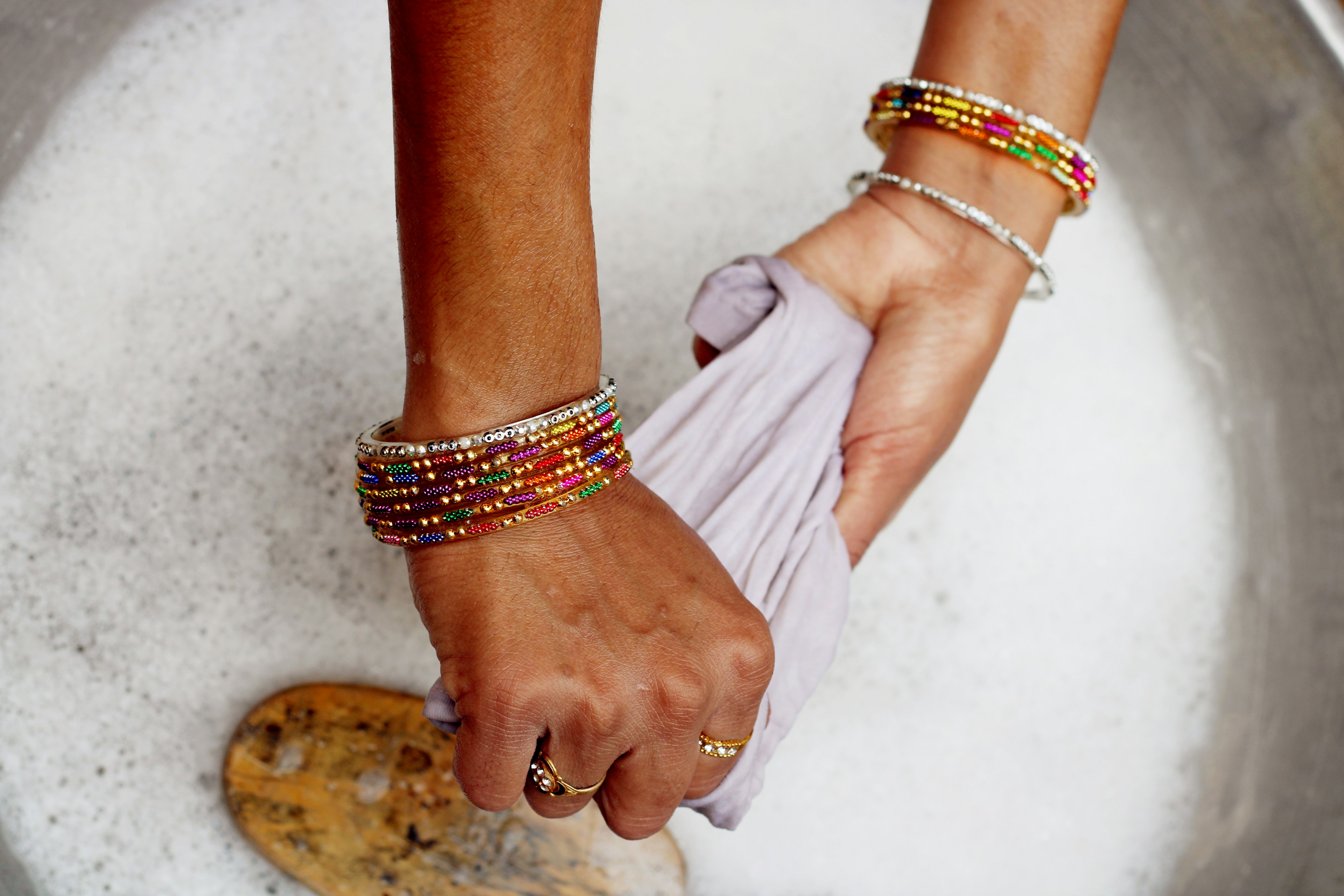 Close up of a woman's hands adorned with colorful bangles and gold rings.