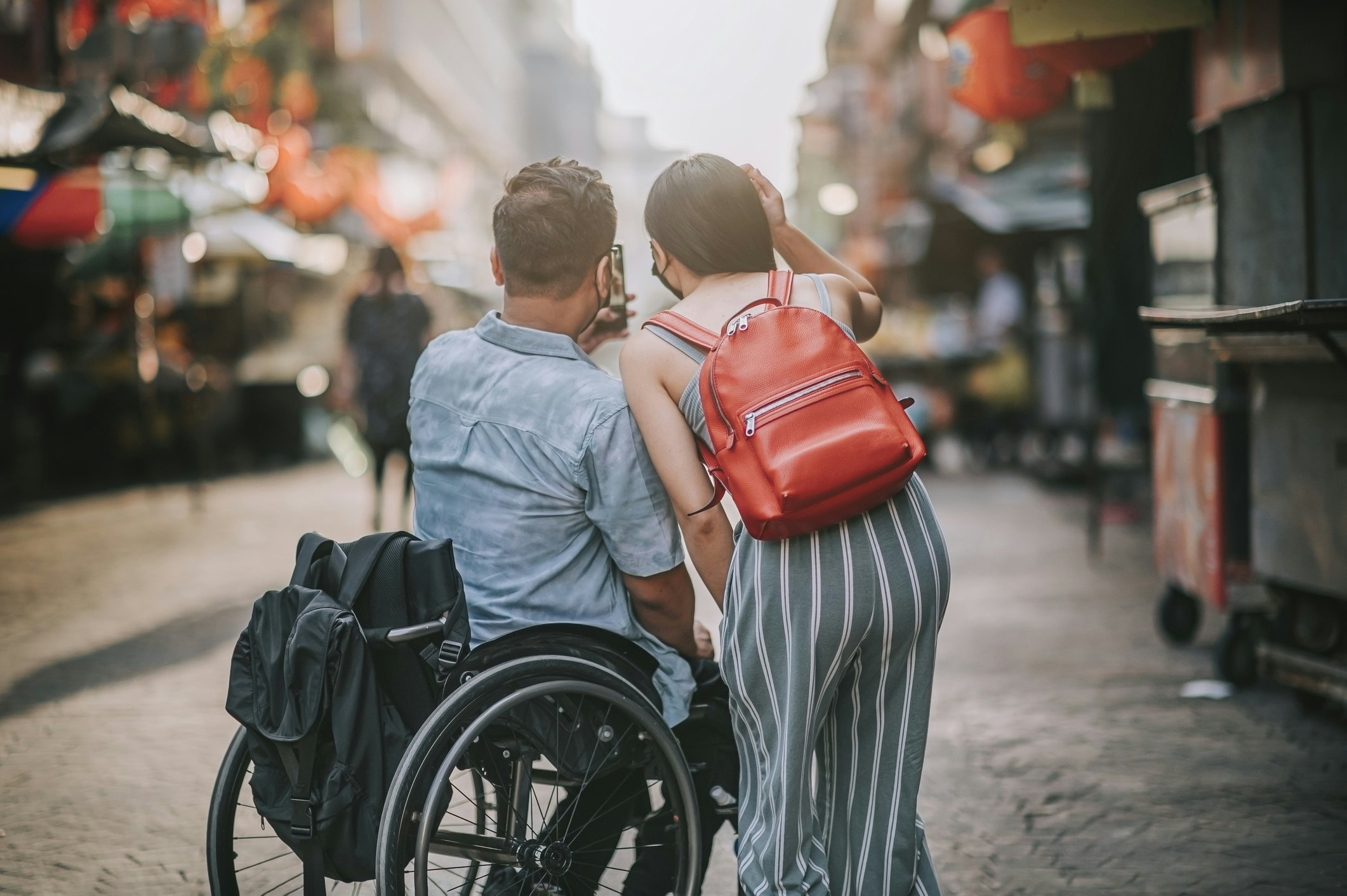 rear view tourist Asian Chinese couple with wheelchair photographing using smart phone at petaling street, kuala lumpur during sunset