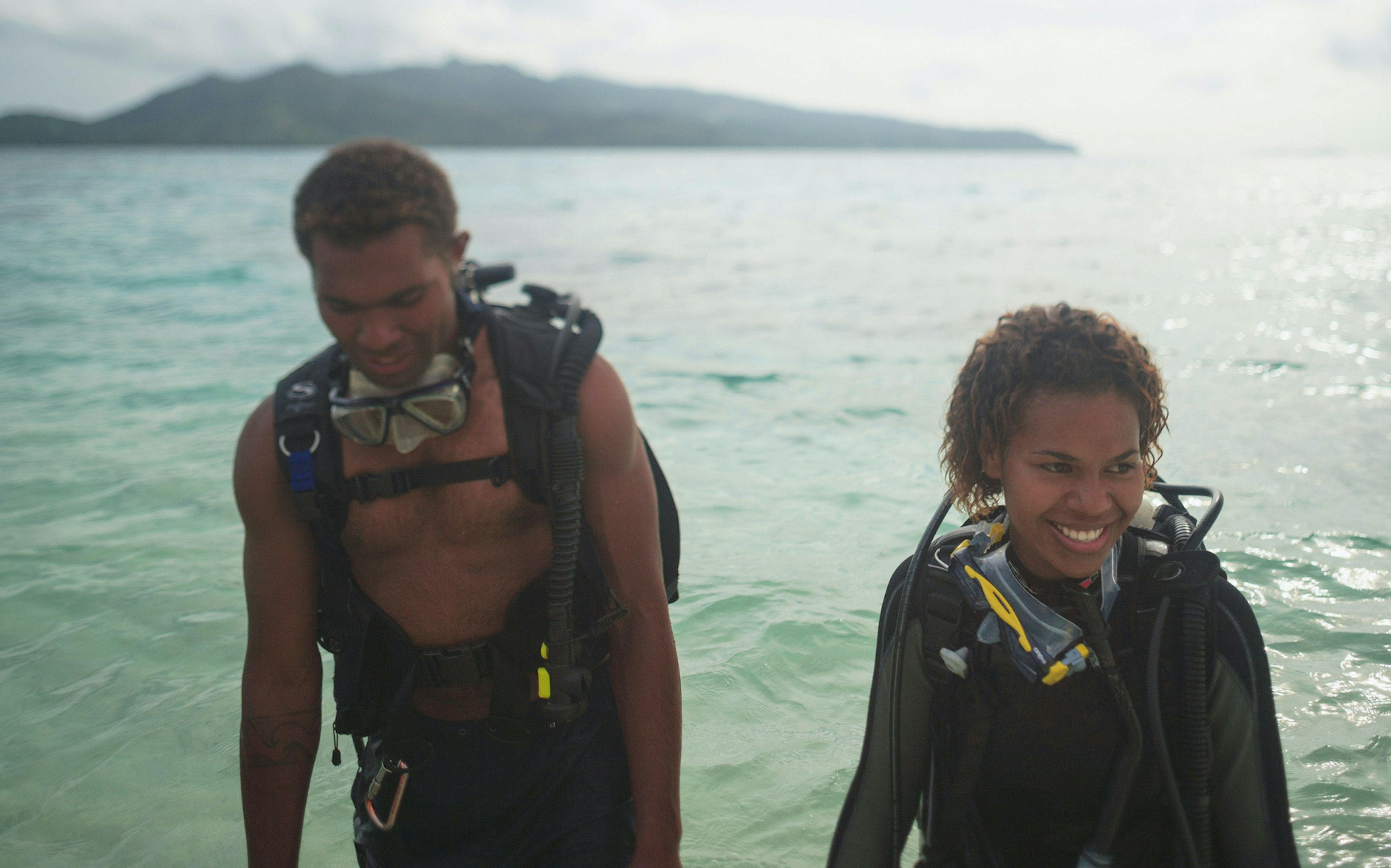 A couple of scuba divers walk out of the ocean in Fiji while smiling