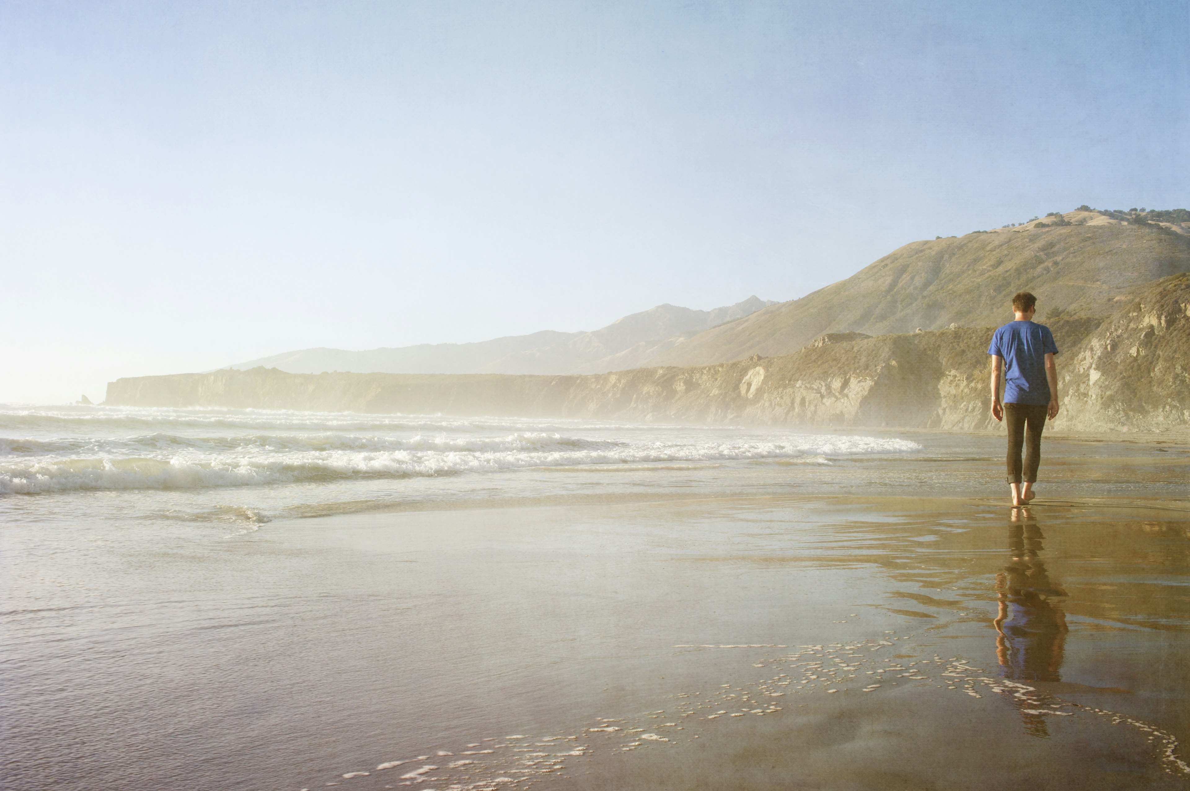 A man walking barefoot along a beach