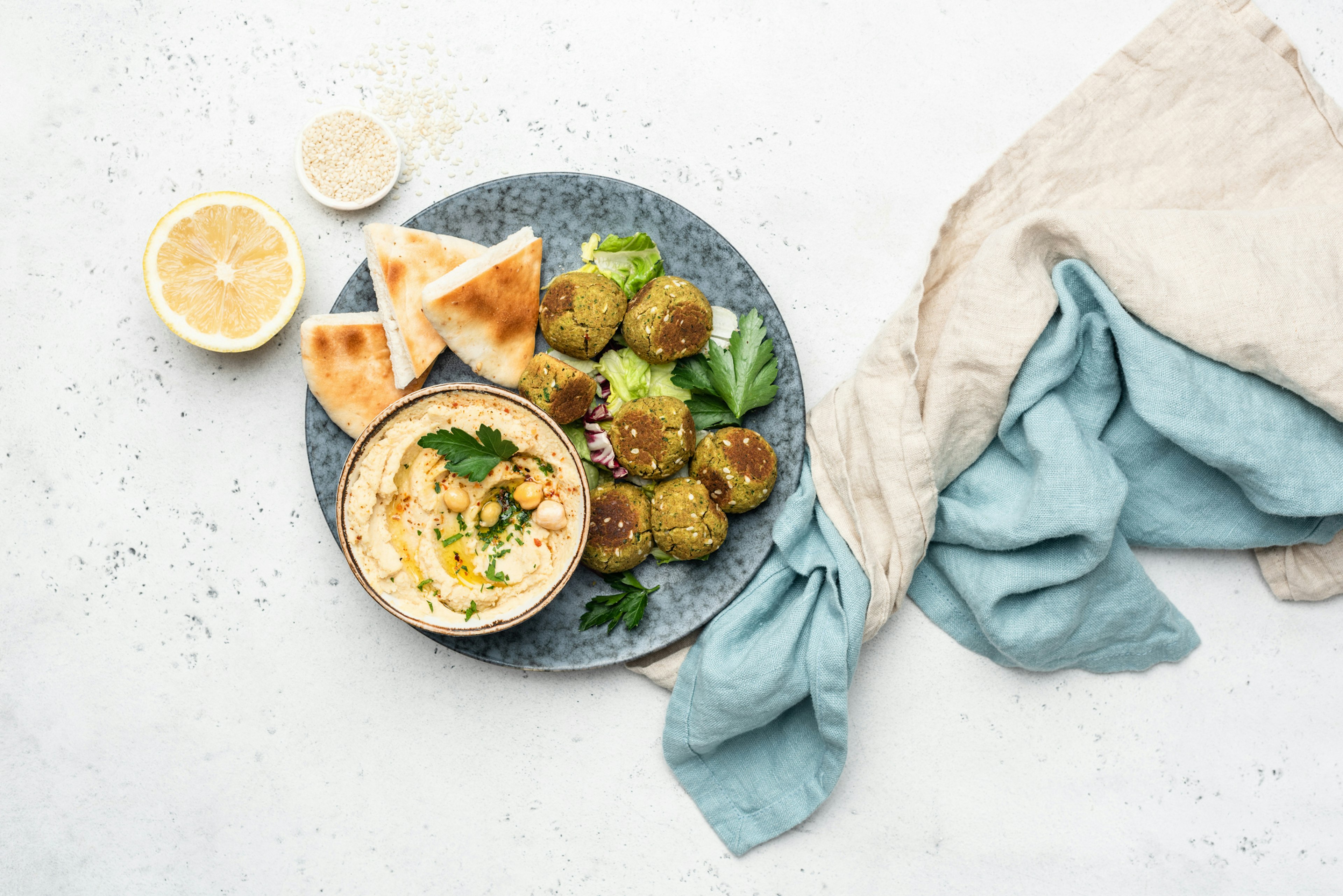 Falafel, hummus and pita bread on a white background with a white and blue cloth twisted to the side