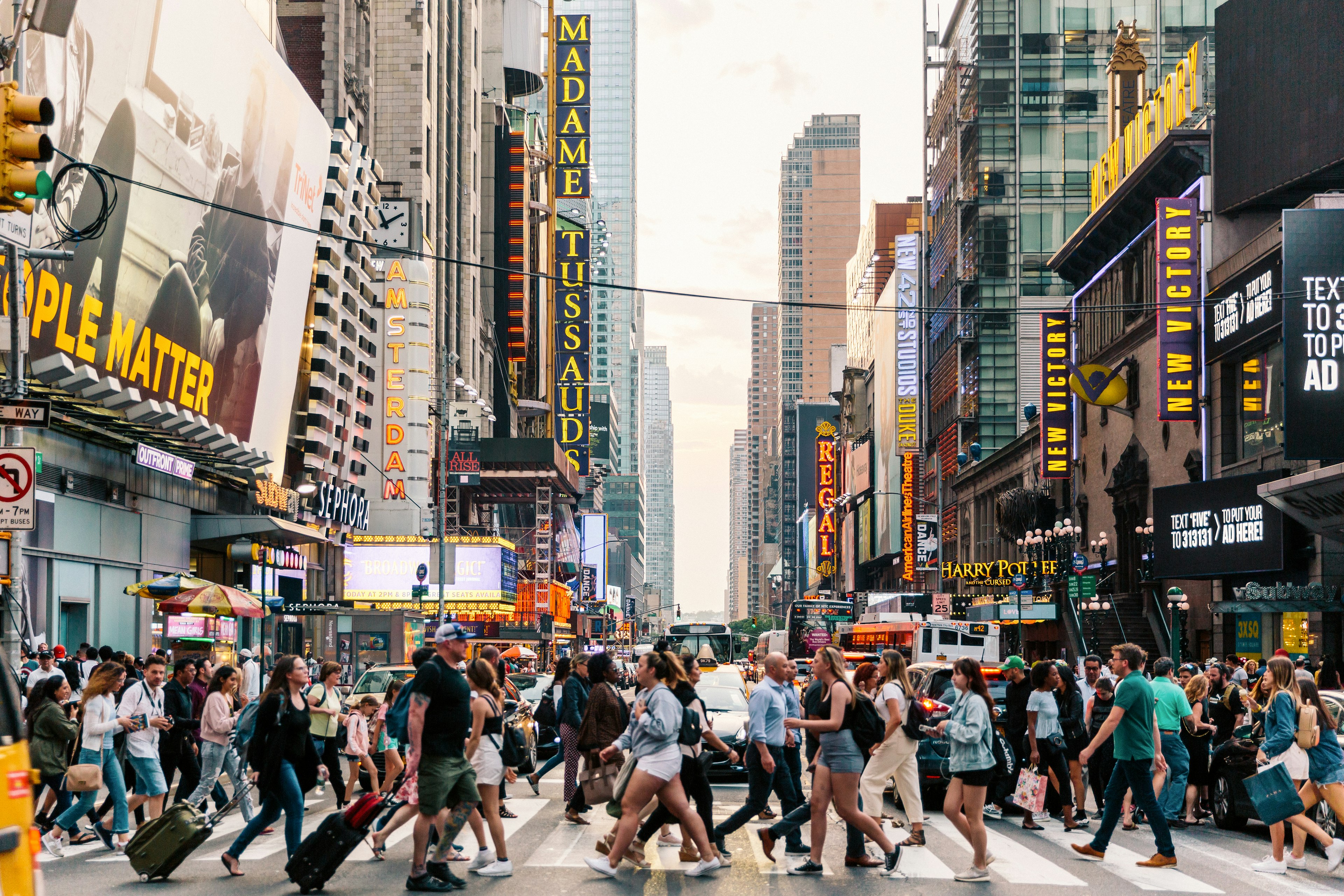 Crowds of people crossing a busy city street lined with theater signs and other entertainment in New York City