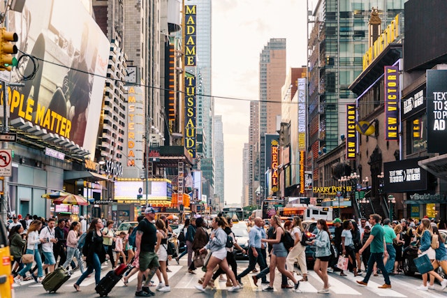Crowds of people crossing a busy city street lined with theater signs and other entertainment in New York City