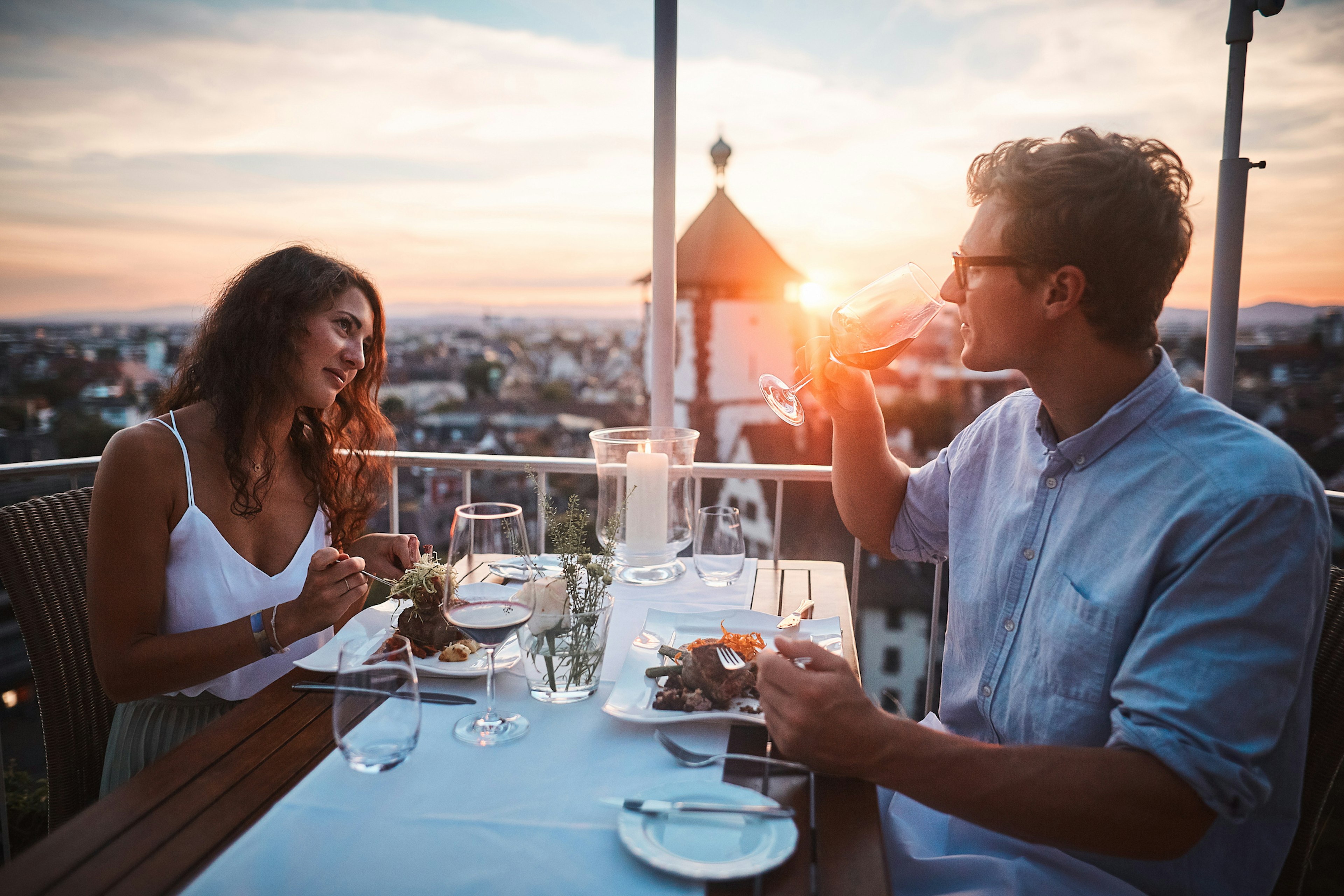 A couple enjoy dinner outdoors as the sun sets behind them over the rooftops of Freiburg