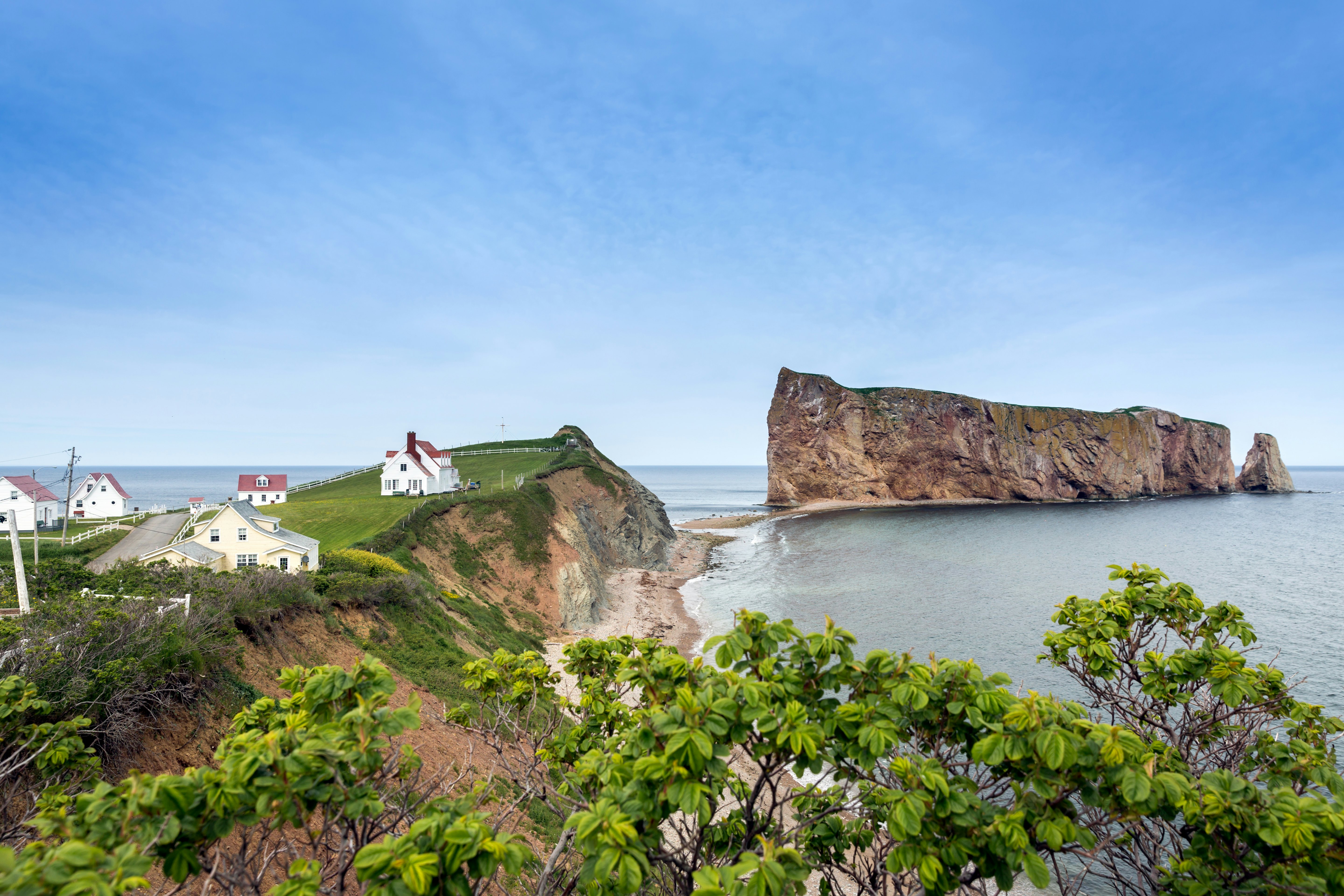 A sheer rock formation just off the tip of the land where it meets the sea. A couple of houses sit exposed to the elements