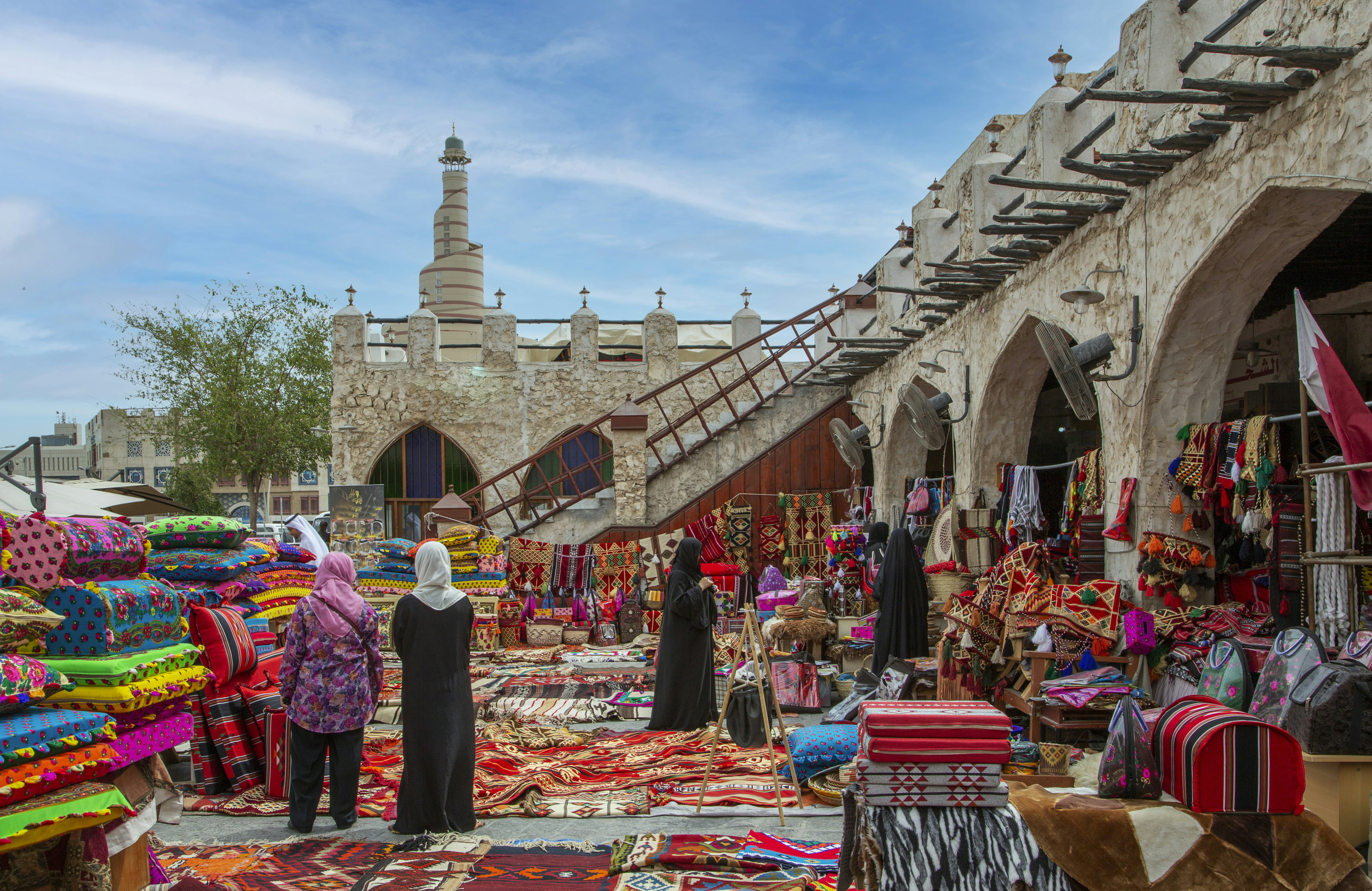 Carpets on sale in old Doha night souk, with Al-Fanar Qatar Islamic Cultural Center in the background.