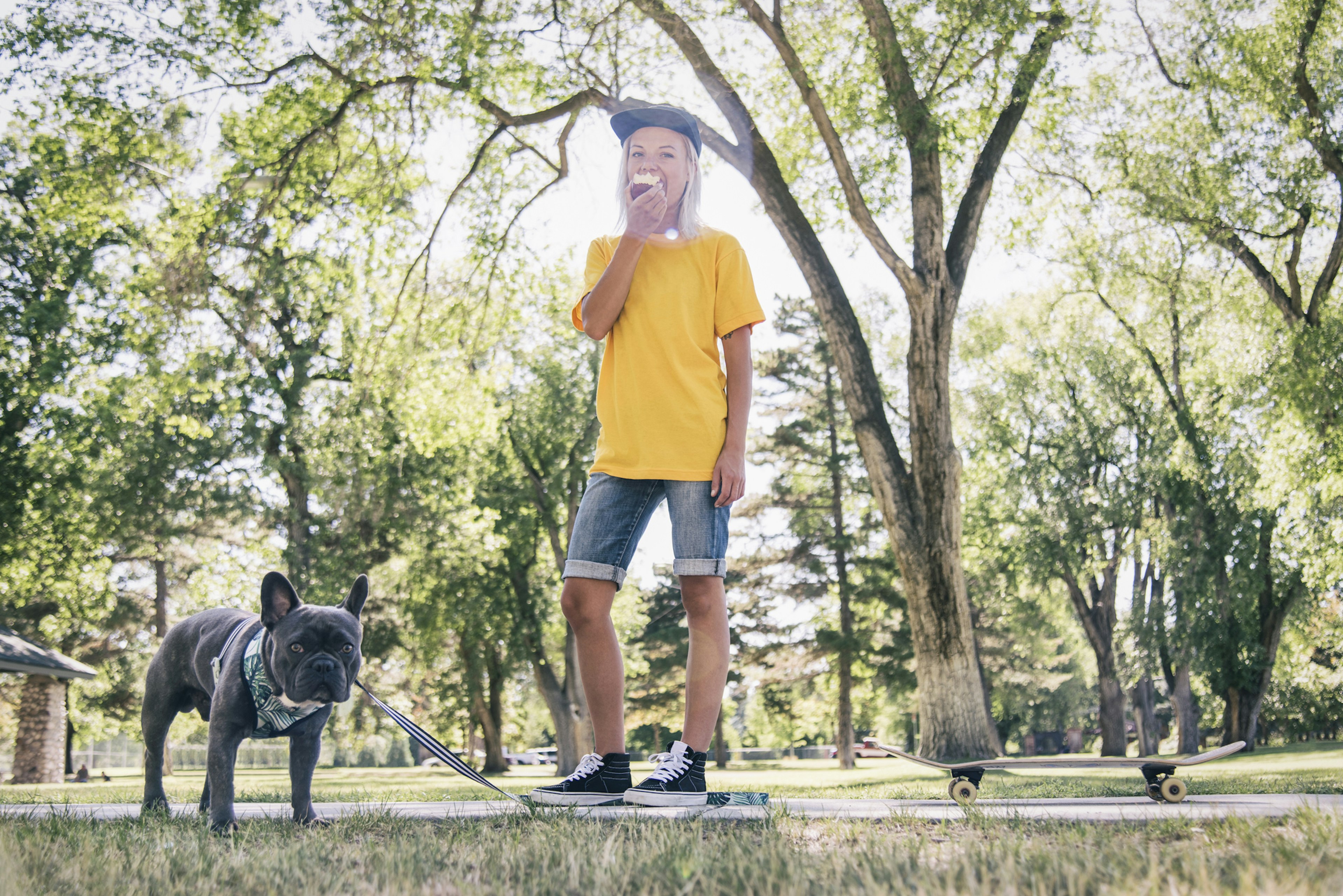 Young woman standing in park with a skateboard next to her and her dog