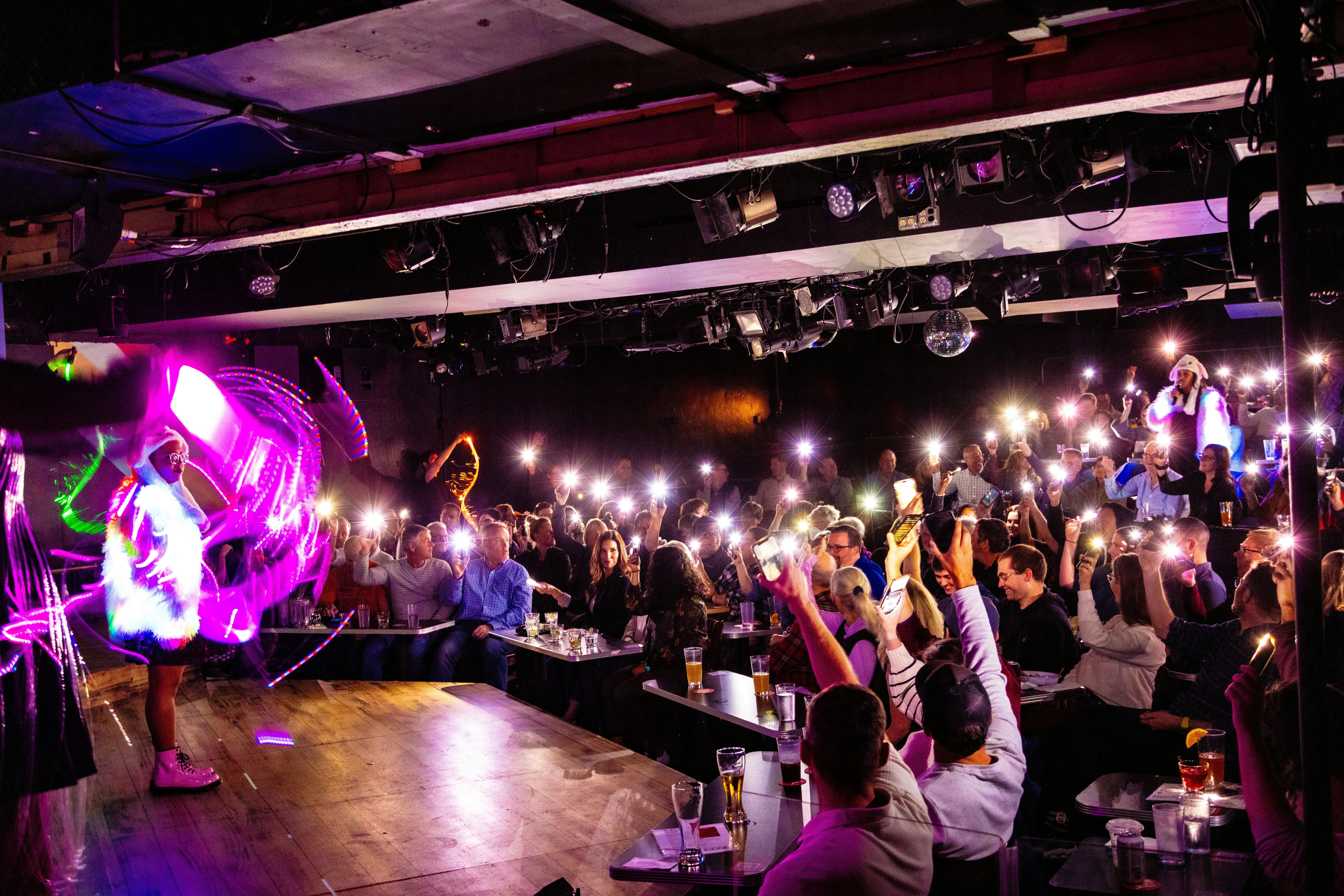 Brittani Yawn and Claudia Martinez performing in reflective outfits as audience members hold up their cell phone torches at Second City, Chicago.