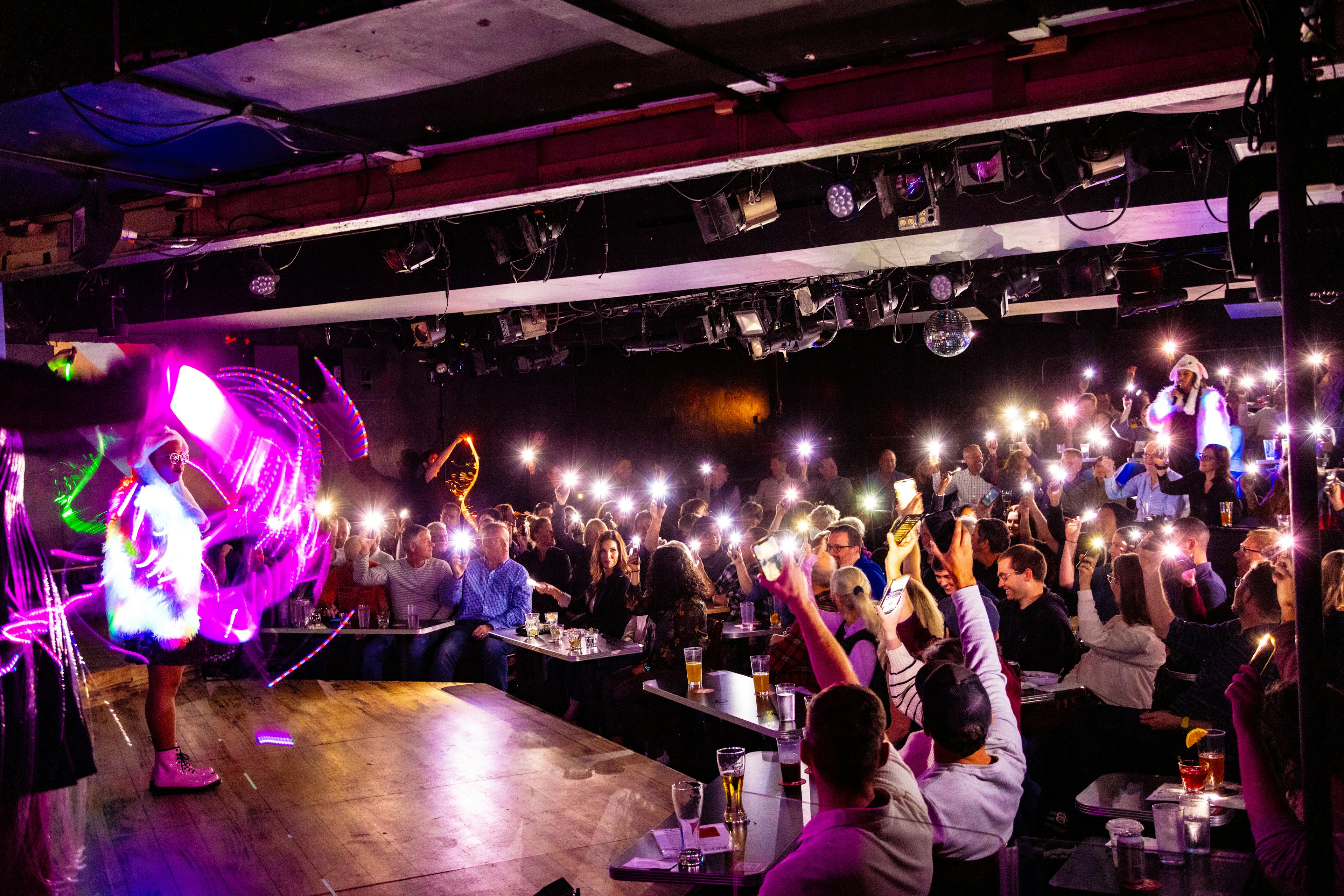 Brittani Yawn and Claudia Martinez performing in reflective outfits as audience members hold up their cell phone torches at Second City, Chicago.