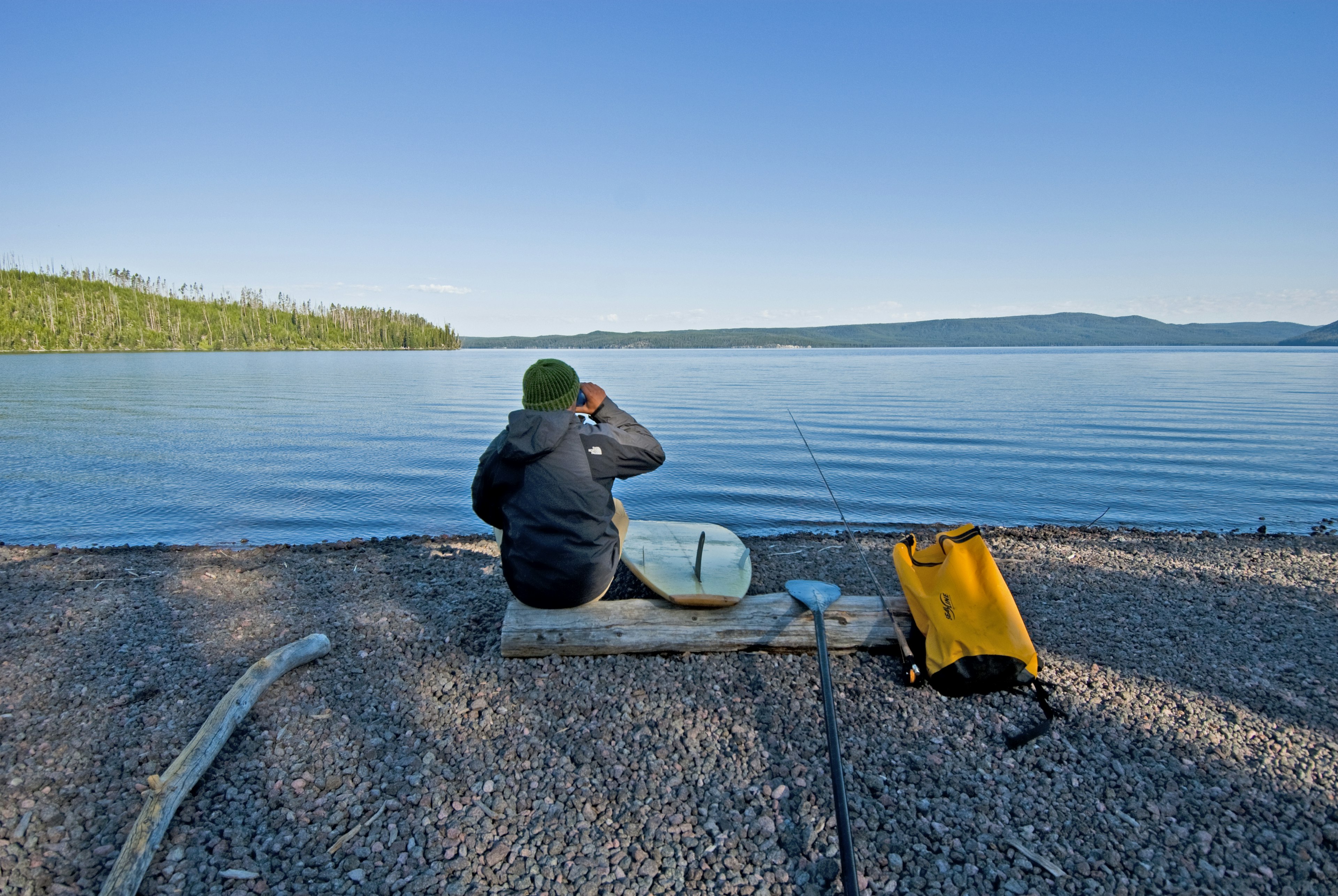 A person sitting with their back to the camera on a log on the banks of Shoshone Lake