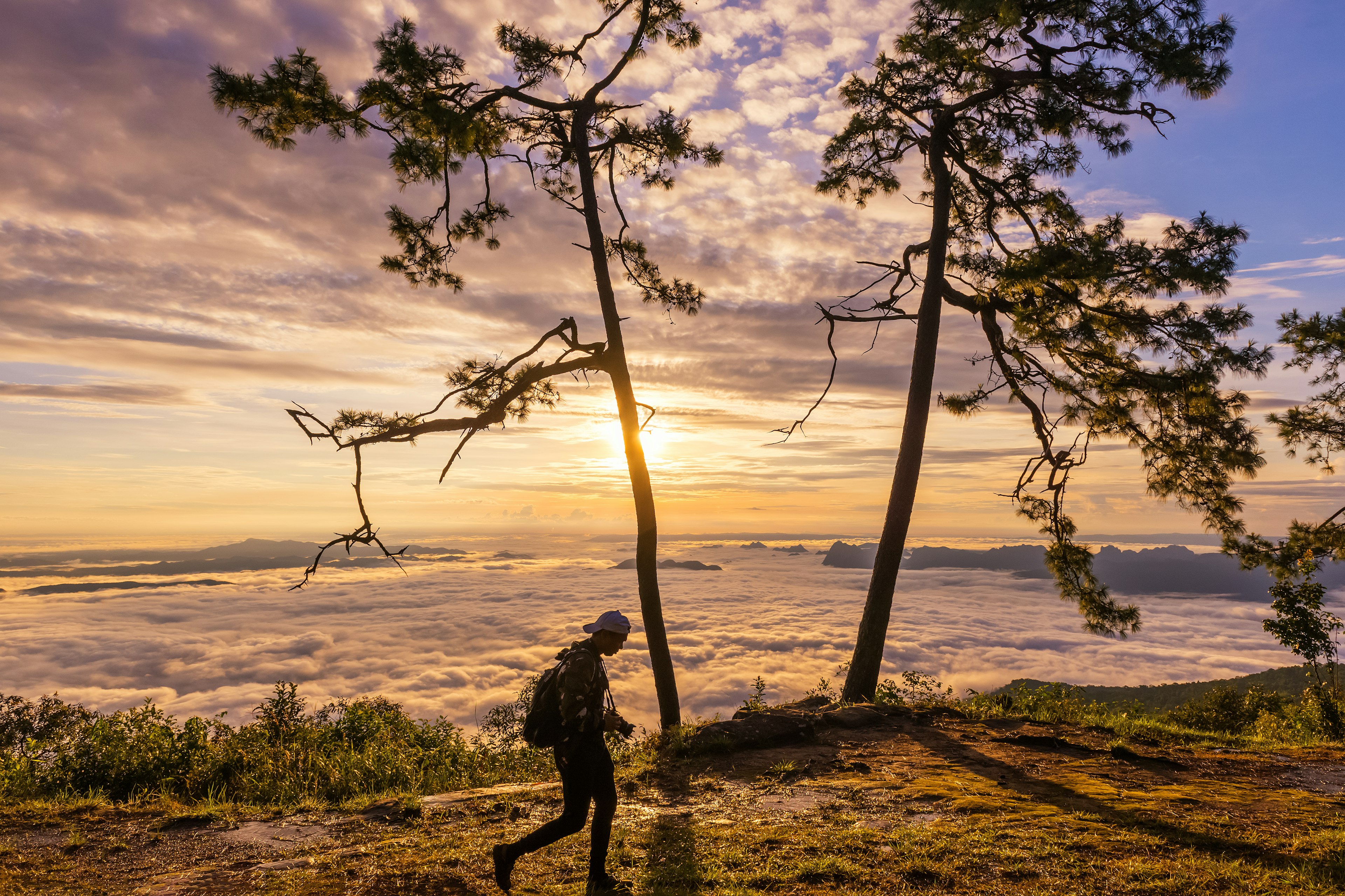 A person in silhouette on the top of a mountain with the setting sun against the clouds creating a ripple effect in the sky